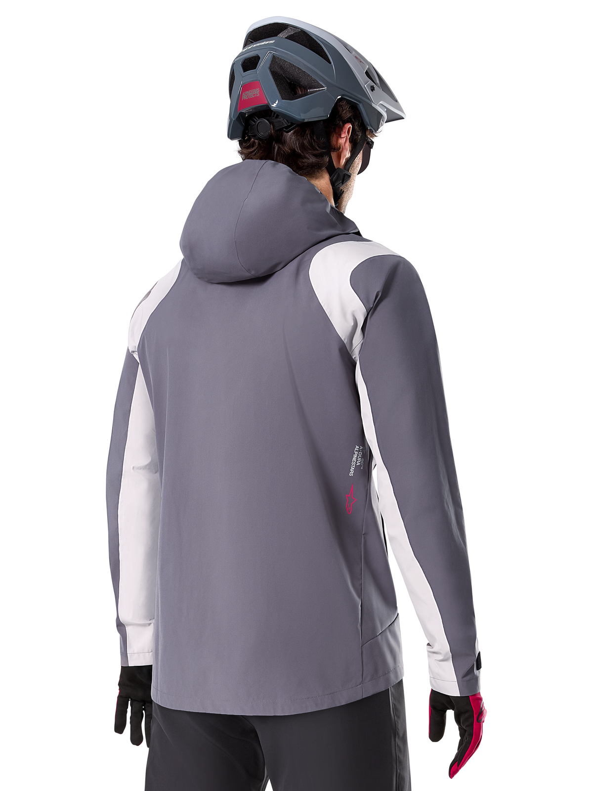Veste de pluie Alpinestars A-Dura, veste de VTT, gris titane foncé, vue de dos avec empiècements gris clair sur les épaules et les bras, détail du logo rouge sur le côté, portée avec un casque de VTT gris et des gants noirs et rouges, vêtement technique de trail