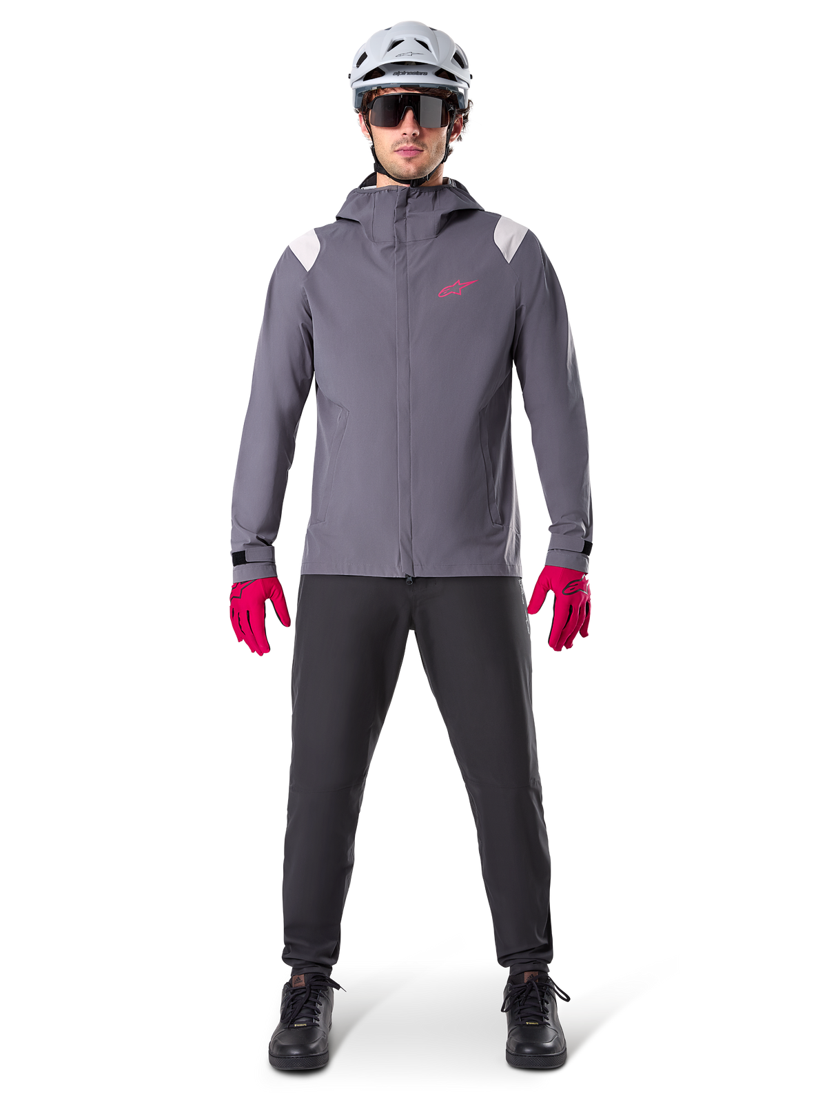 Veste de pluie Alpinestars A-Dura, veste de VTT, gris titane foncé avec logo rose, portée avec un casque de VTT gris et des gants rose vif, membrane protectrice à 2,5 couches pour le cyclisme par temps humide