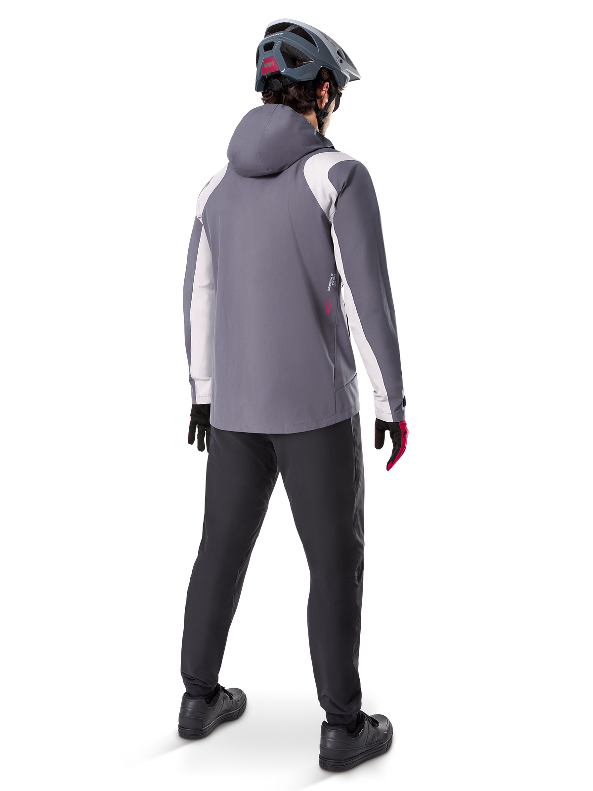 Veste de pluie Alpinestars A-Dura, veste de VTT, gris titane foncé avec empiècements blancs, vue arrière d'un cycliste portant un casque gris assorti et un pantalon noir, équipement technique pour temps humide