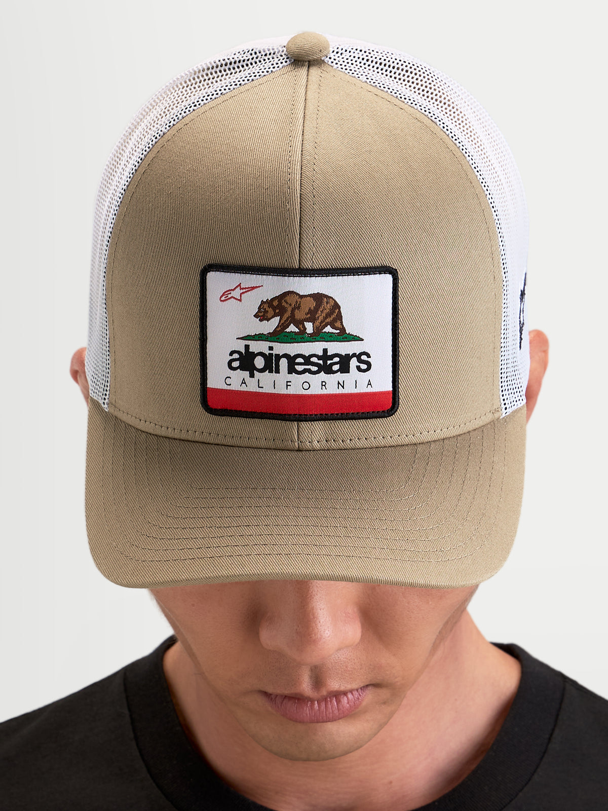 Alpinestars Casquette Cali 2.0, casquette trucker sportswear, kaki et blanche, dotée d'une calotte structurée en sergé avec un écusson ours de Californie, visière incurvée et arrière en maille respirante porté par un modèle