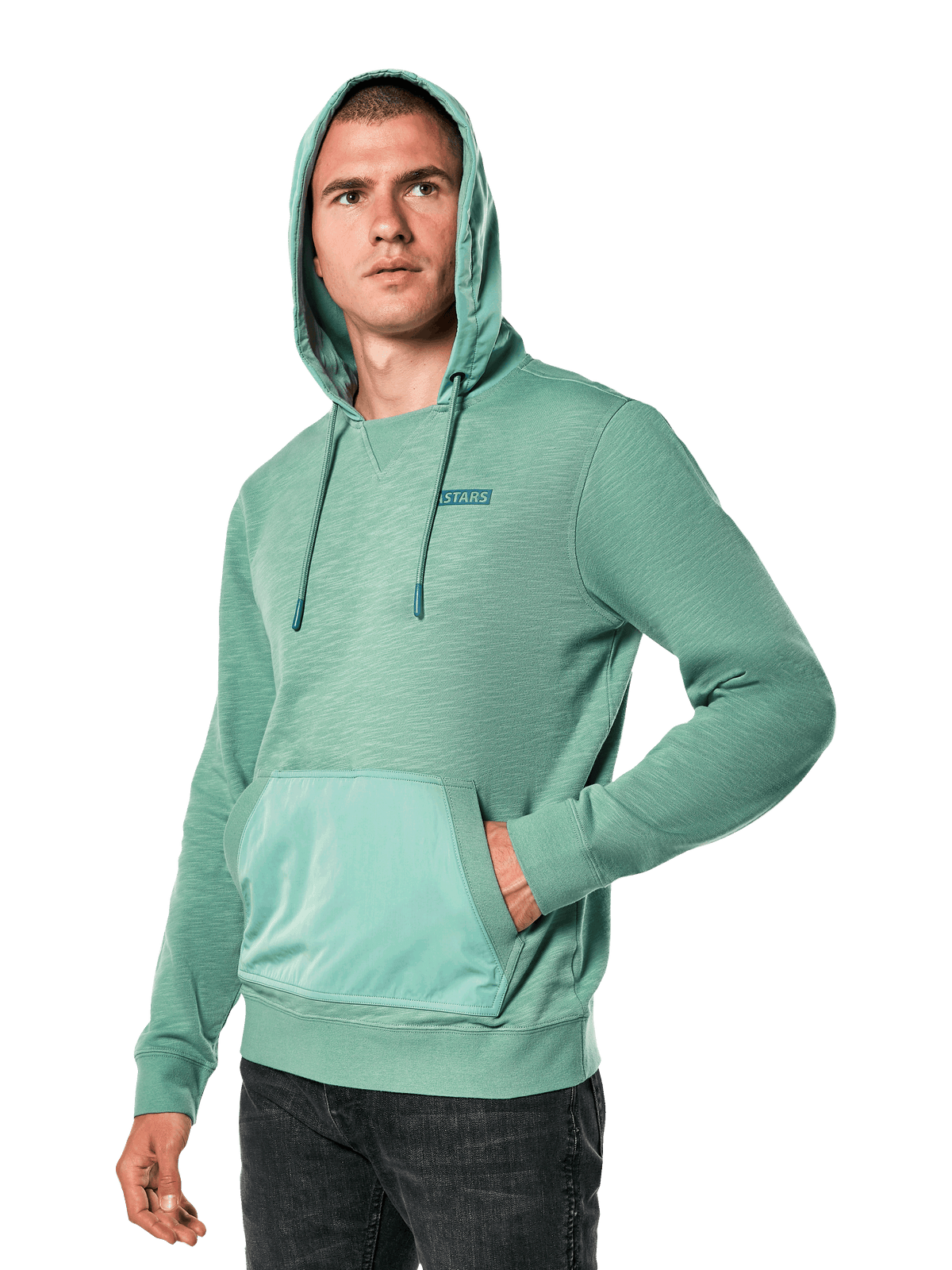 Alpinestars Rooted Hoodie, sweat-shirt vert en molleton flammé avec capuche superposée et poche kangourou, petit logo STARS sur la poitrine, porté par un mannequin avec la capuche relevée et une main dans la poche, style streetwear décontracté d'inspiration sport automobile