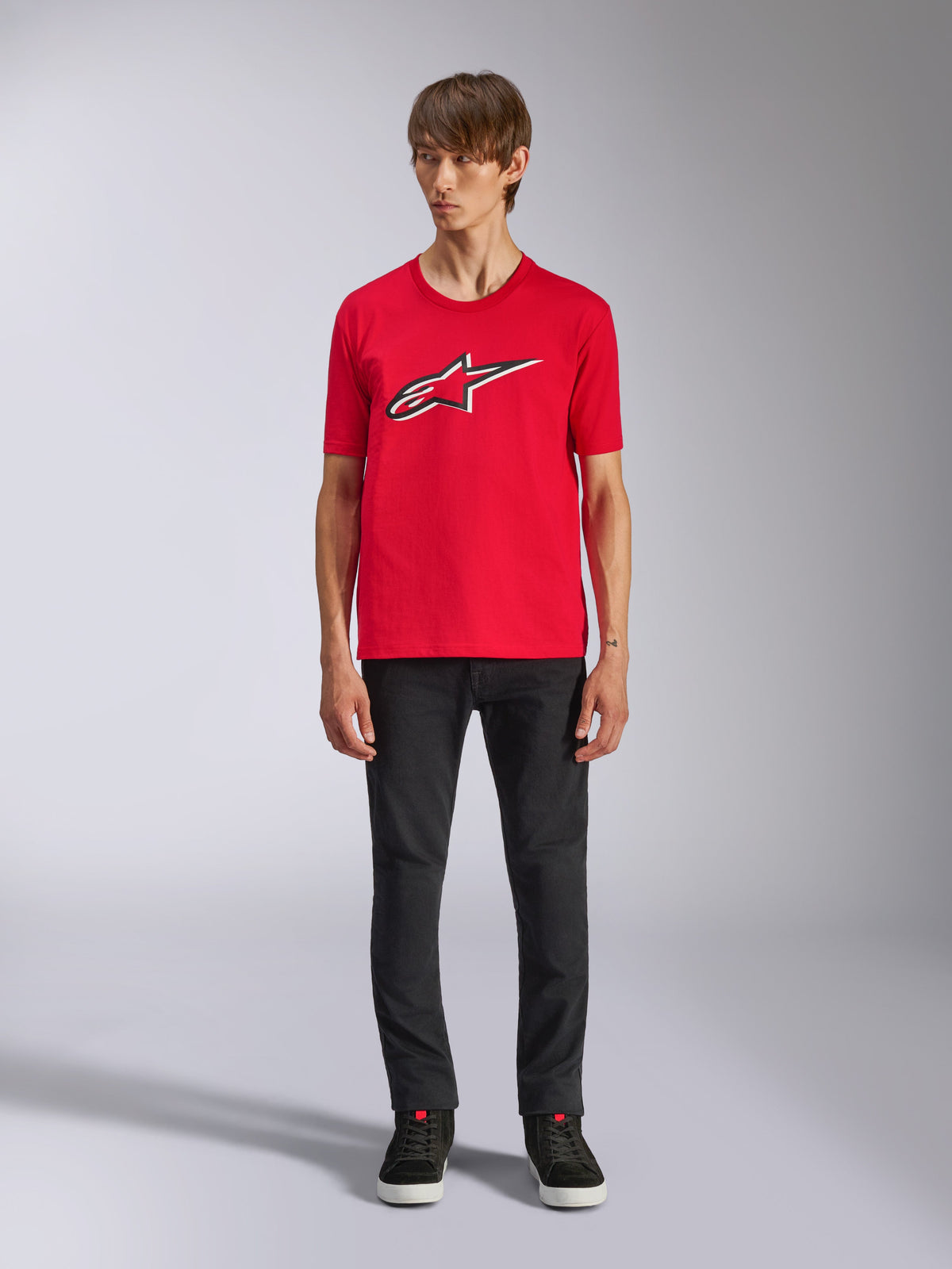 T-shirt Alpinestars Ageless Shadow CSF, t-shirt à manches courtes, rouge, logo Ageless à l'avant avec contours blancs et noirs, porté par un mannequin avec un pantalon noir et des baskets, vêtement streetwear décontracté motorsport