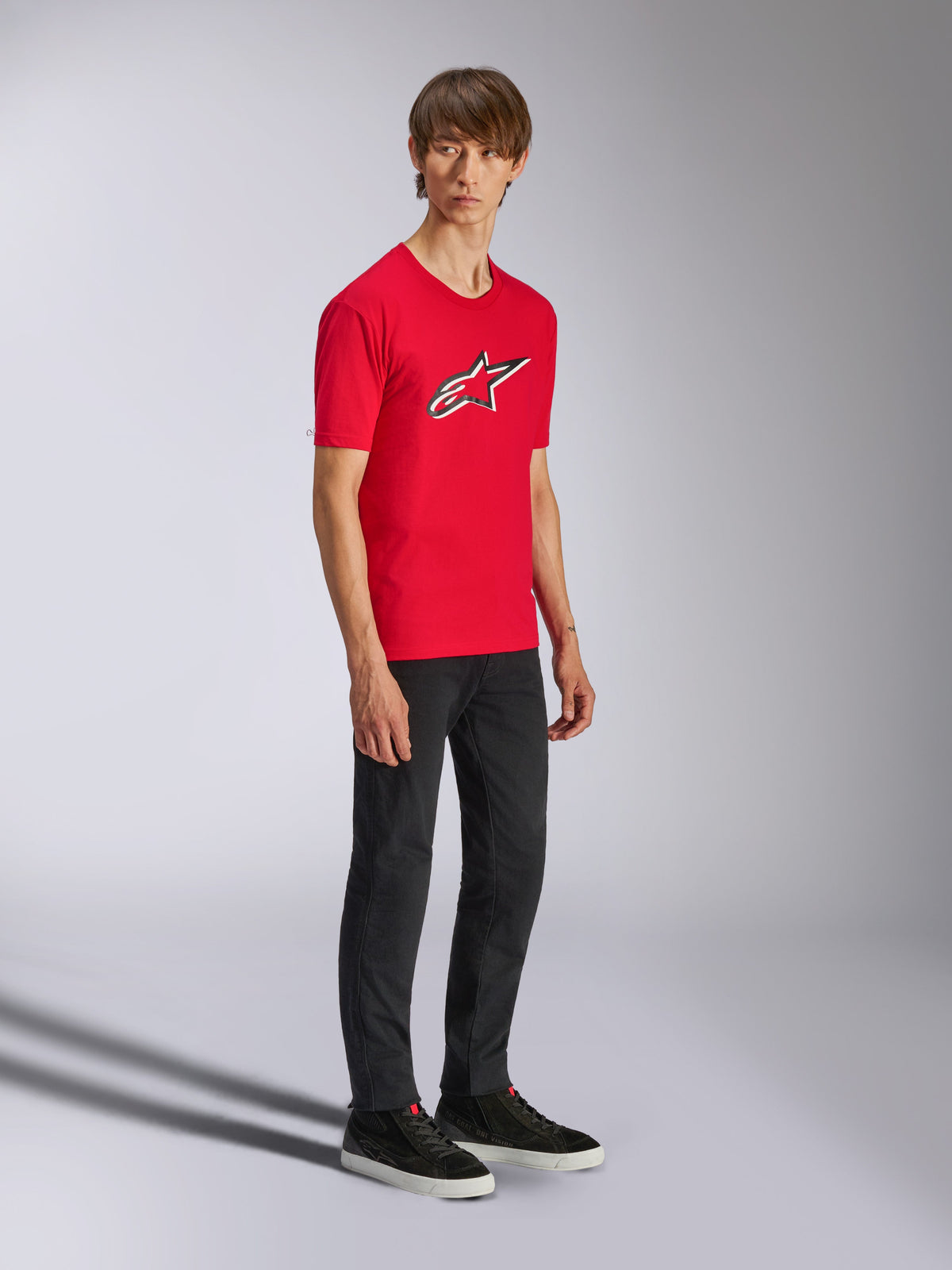 T-shirt Alpinestars Ageless Shadow CSF, t-shirt rouge à manches courtes, arborant un grand logo Ageless sur la poitrine, porté par un mannequin avec un pantalon noir et des baskets, style streetwear motorsport décontracté