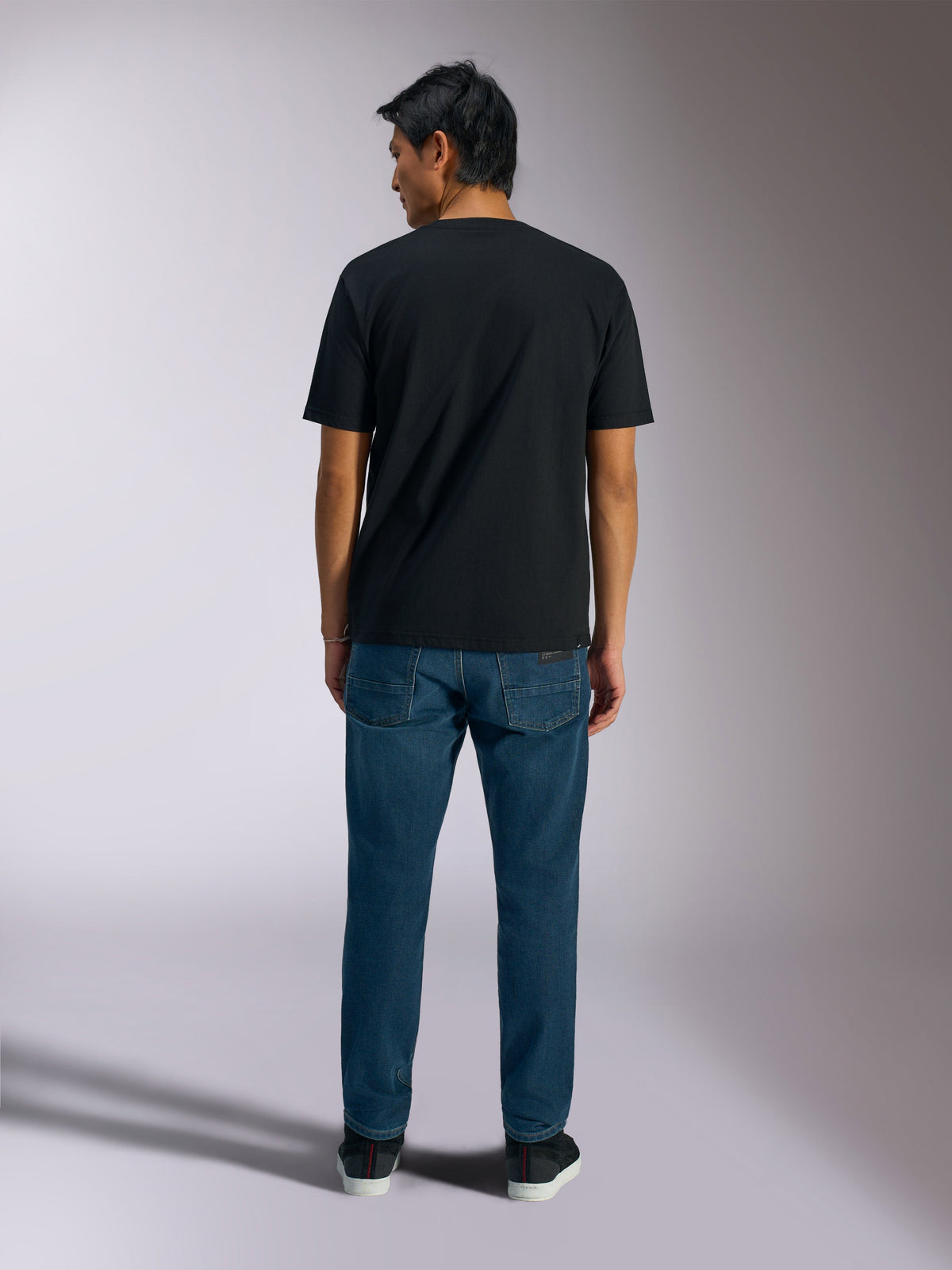 Alpinestars Ageless Shadow CSF Tee, t-shirt à manches courtes, noir, vue de dos, porté avec un jean bleu, streetwear décontracté motorsport