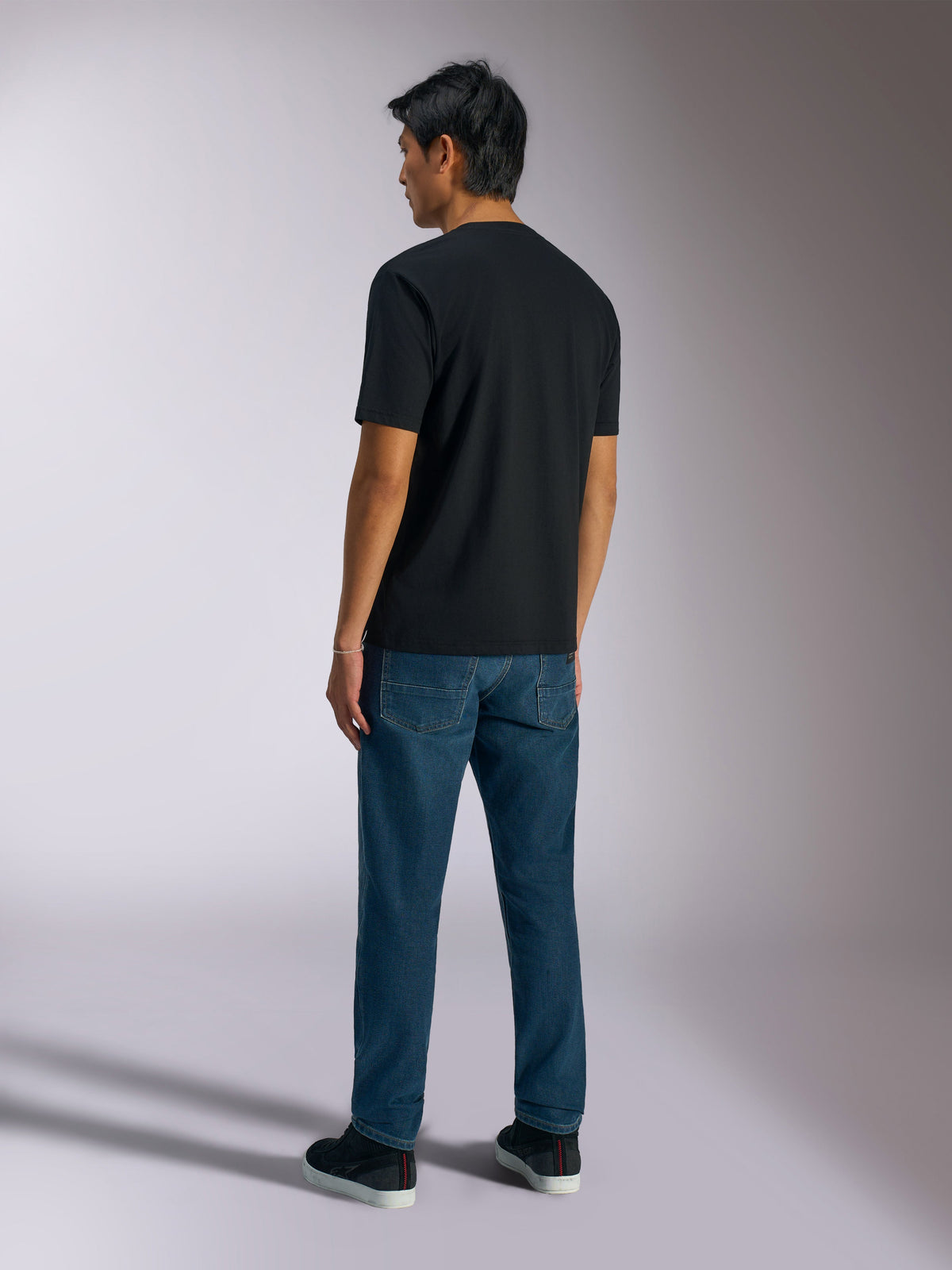 T-shirt Alpinestars Ageless Shadow CSF, t-shirt à manches courtes, noir, vue de dos, porté avec un jean bleu et des baskets noires, streetwear décontracté d'inspiration sport automobile