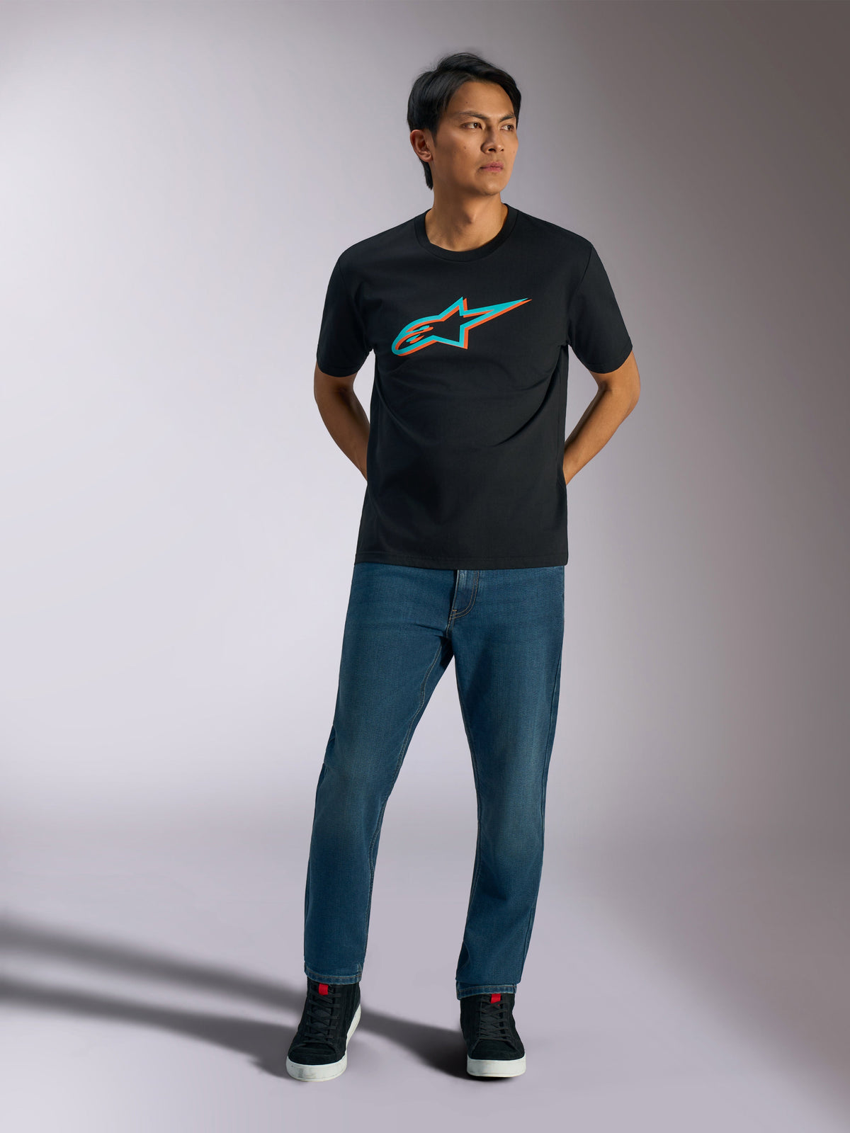Alpinestars Ageless Shadow CSF Tee, t-shirt à manches courtes, noir, logo Ageless effet ombre turquoise et orange sur la poitrine, porté par un mannequin avec un jean bleu et des chaussures noires, style streetwear décontracté