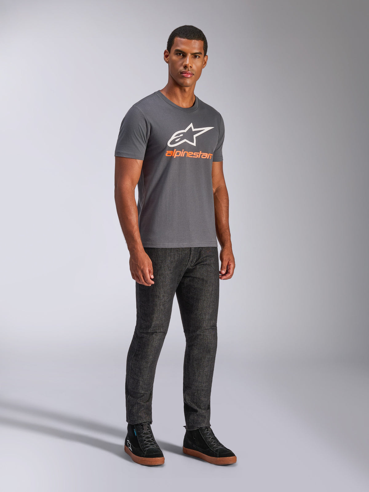 T-shirt Alpinestars Always 2.0 CSF, t-shirt à manches courtes, gris anthracite, logo A-star blanc avec marquage orange, style streetwear décontracté porté avec un jean foncé et des baskets noires