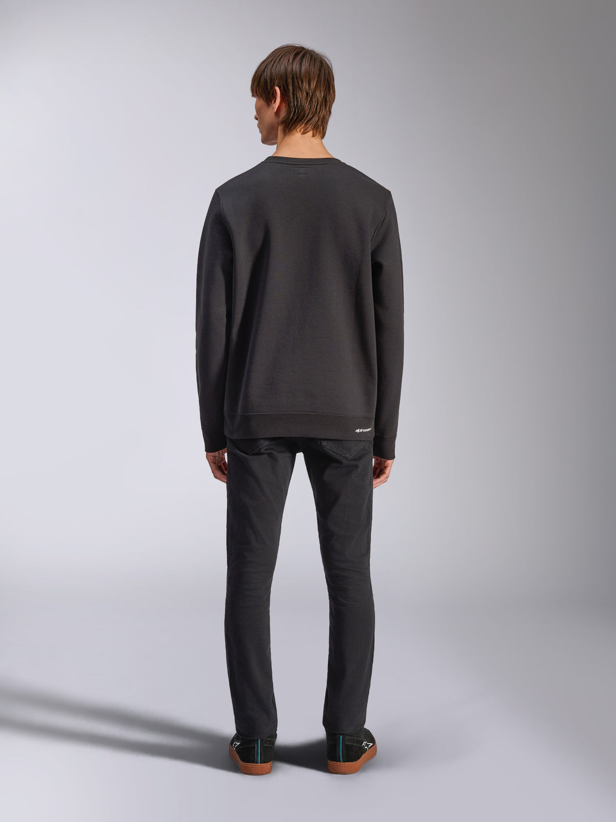 Alpinestars Positive Crew, sweatshirt noir, vue arrière sur un mannequin homme, porté avec un jean noir et des baskets décontractées, doté de poignets et d'un ourlet côtelés, streetwear d'inspiration sport mécanique