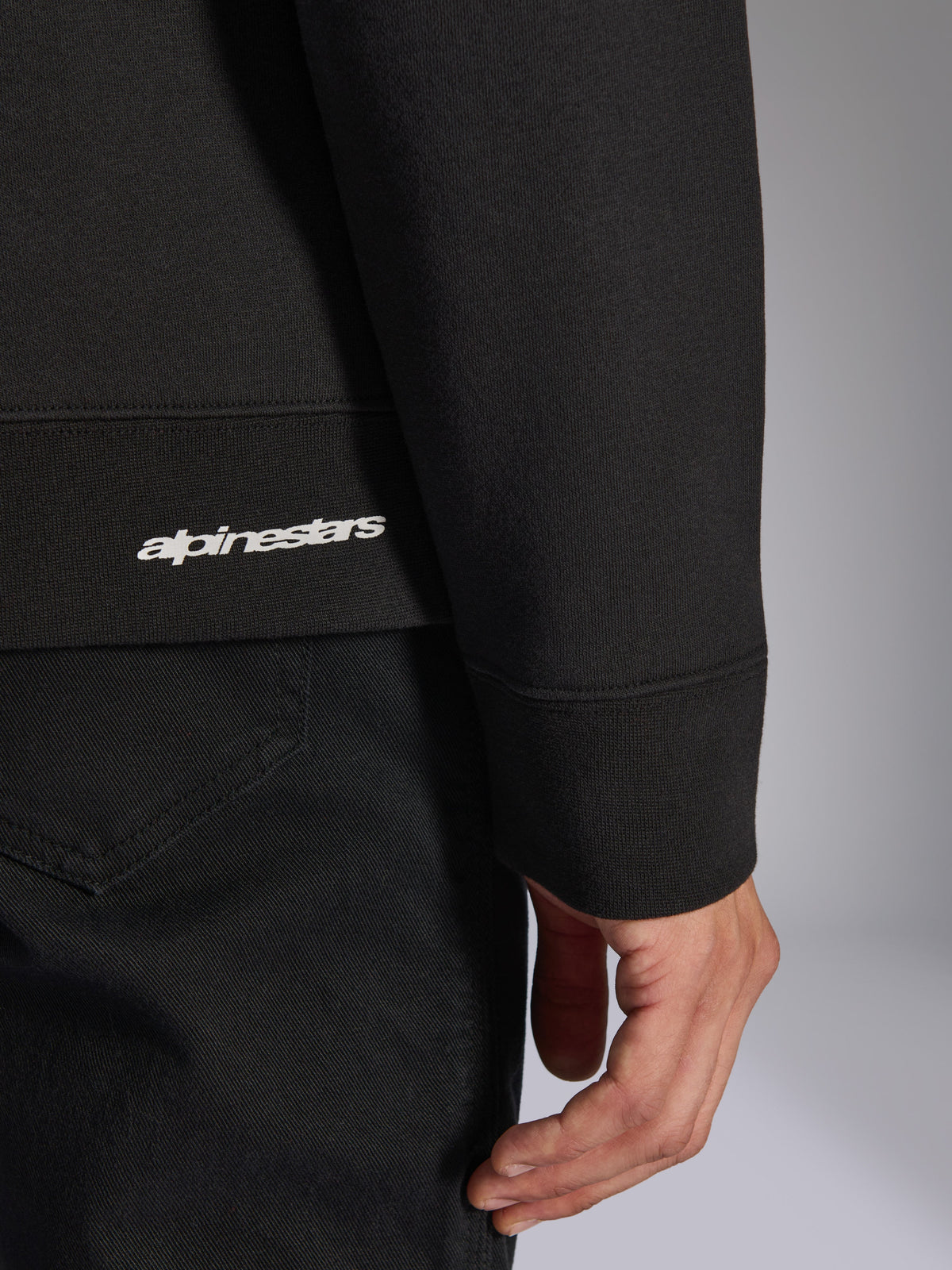 Alpinestars Positive Crew, sweatshirt noir, gros plan sur l'ourlet côtelé et le poignet avec logo Alpinestars blanc, texture de tissu premium, vêtement de sport décontracté d'inspiration sport automobile