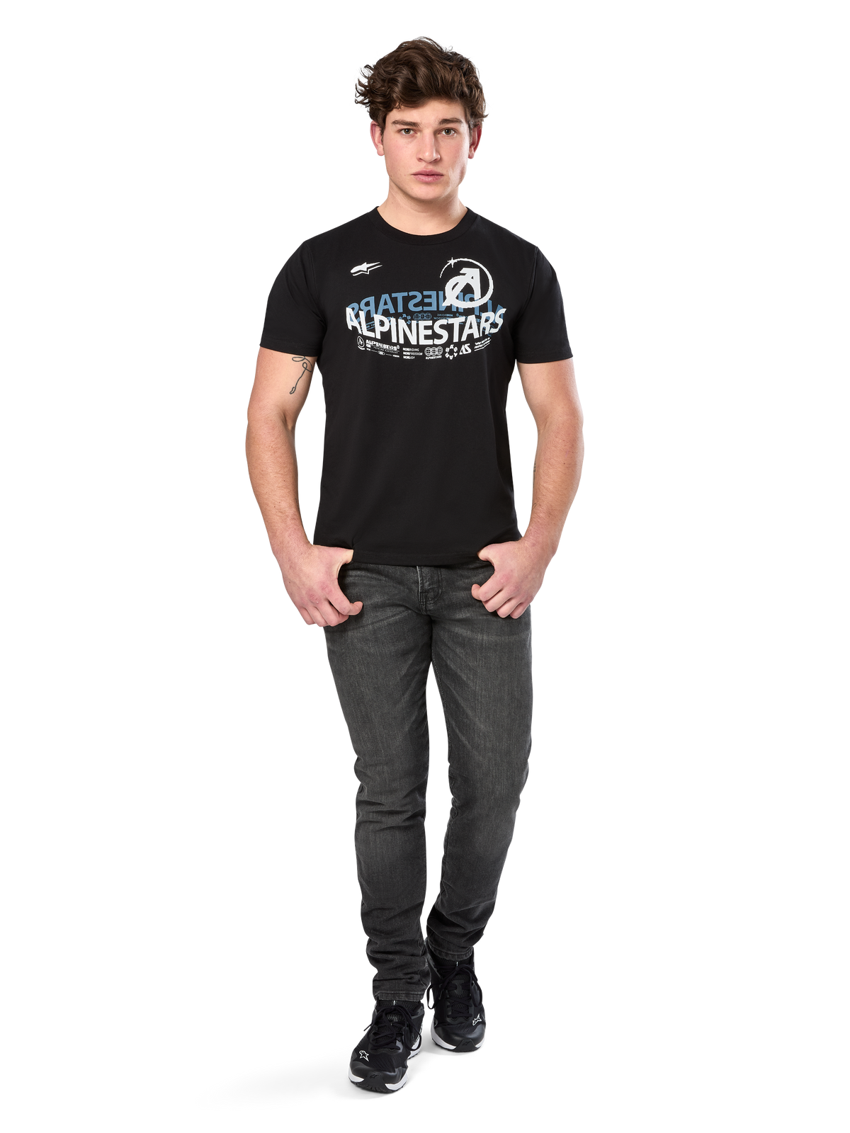 T-shirt Alpinestars Semicircle CSF, t-shirt à manches courtes, noir, graphique incurvé blanc et bleu clair sur la poitrine, porté par un mannequin avec un jean gris foncé et des baskets noires, streetwear motorsport décontracté