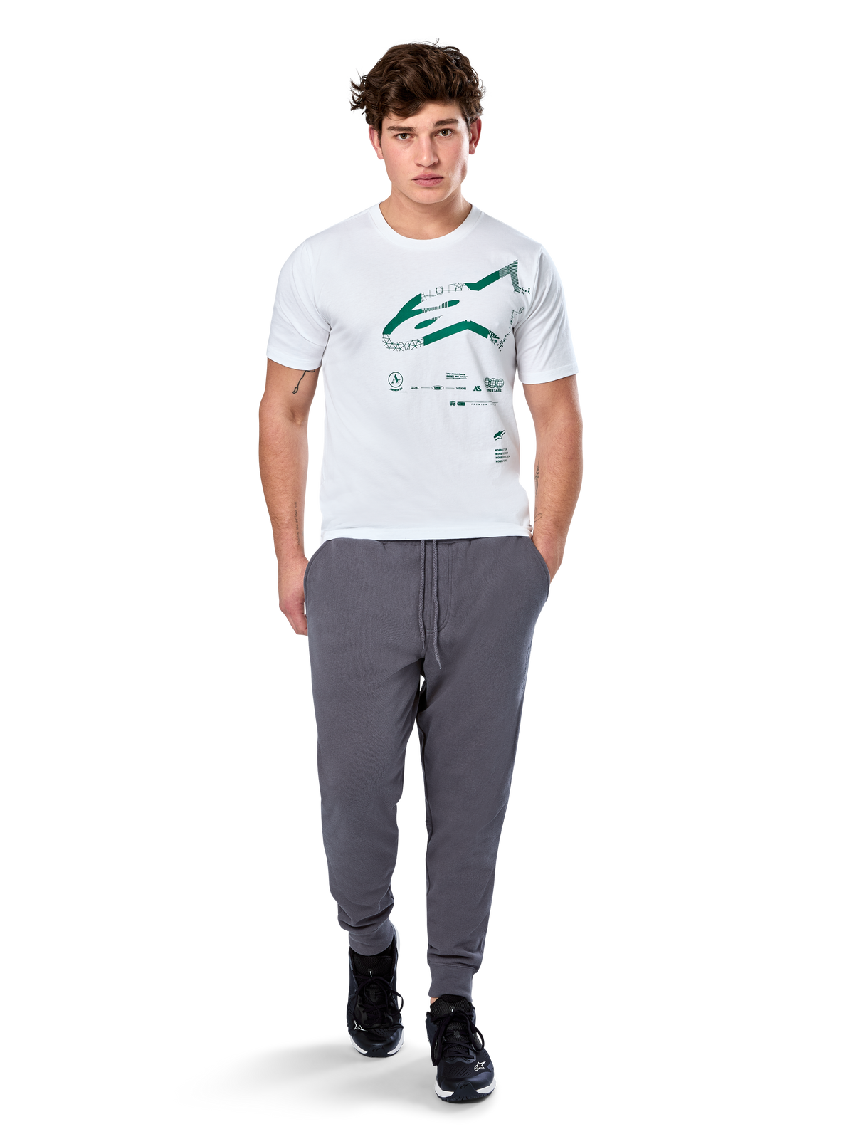 T-shirt Alpinestars Geografica CSF, t-shirt à manches courtes, blanc, logo Astars vert avec graphique géographique multi-tech, porté avec un pantalon de jogging gris et des baskets noires, streetwear motorsport décontracté