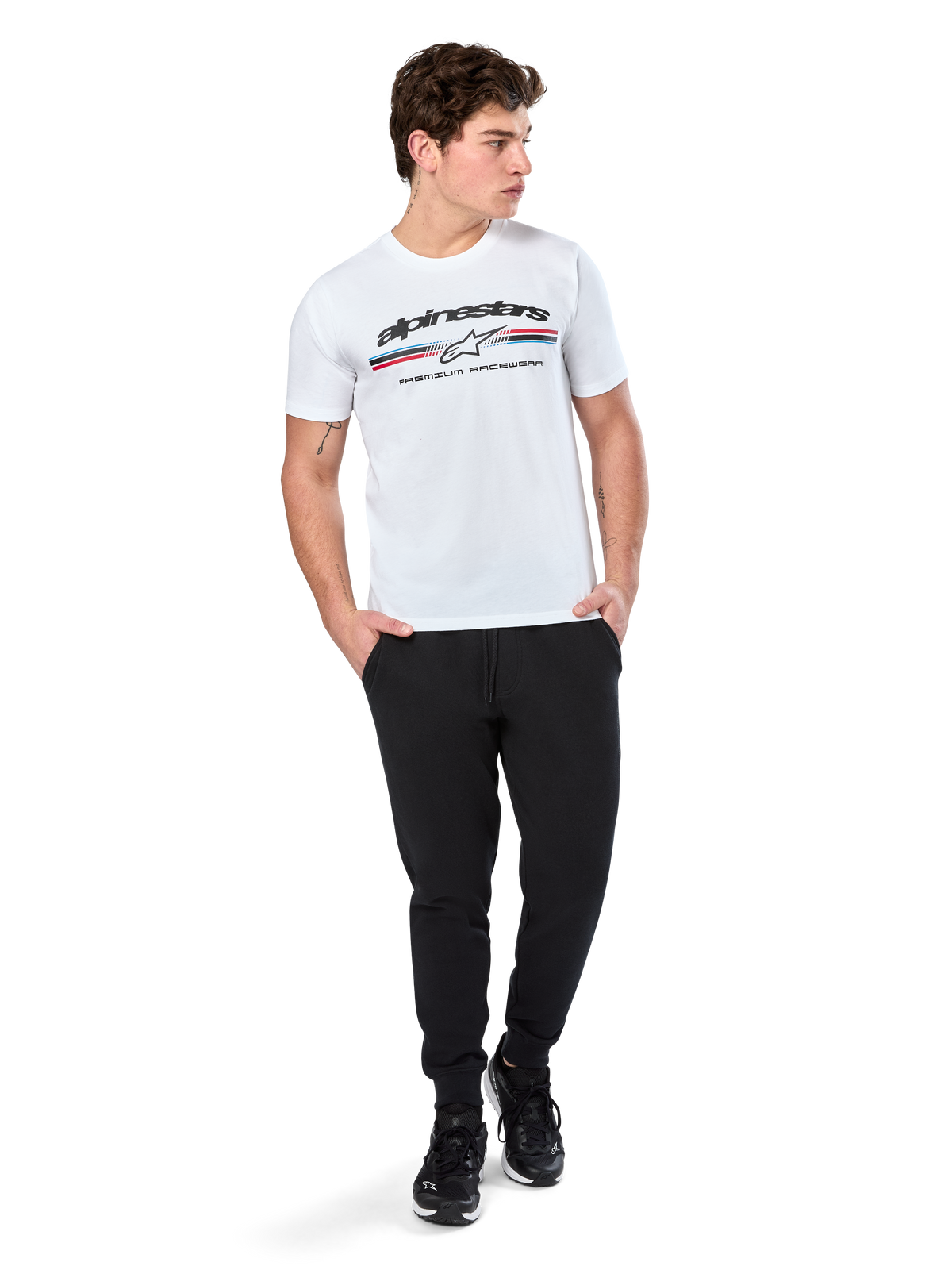 T-shirt Alpinestars Prevail CSF, T-shirt à manches courtes, blanc, arborant un logo frontal à rayures tricolores style paddock avec marquage Alpinestars, porté par un mannequin avec un pantalon de jogging noir et des baskets noires, streetwear décontracté de sport automobile