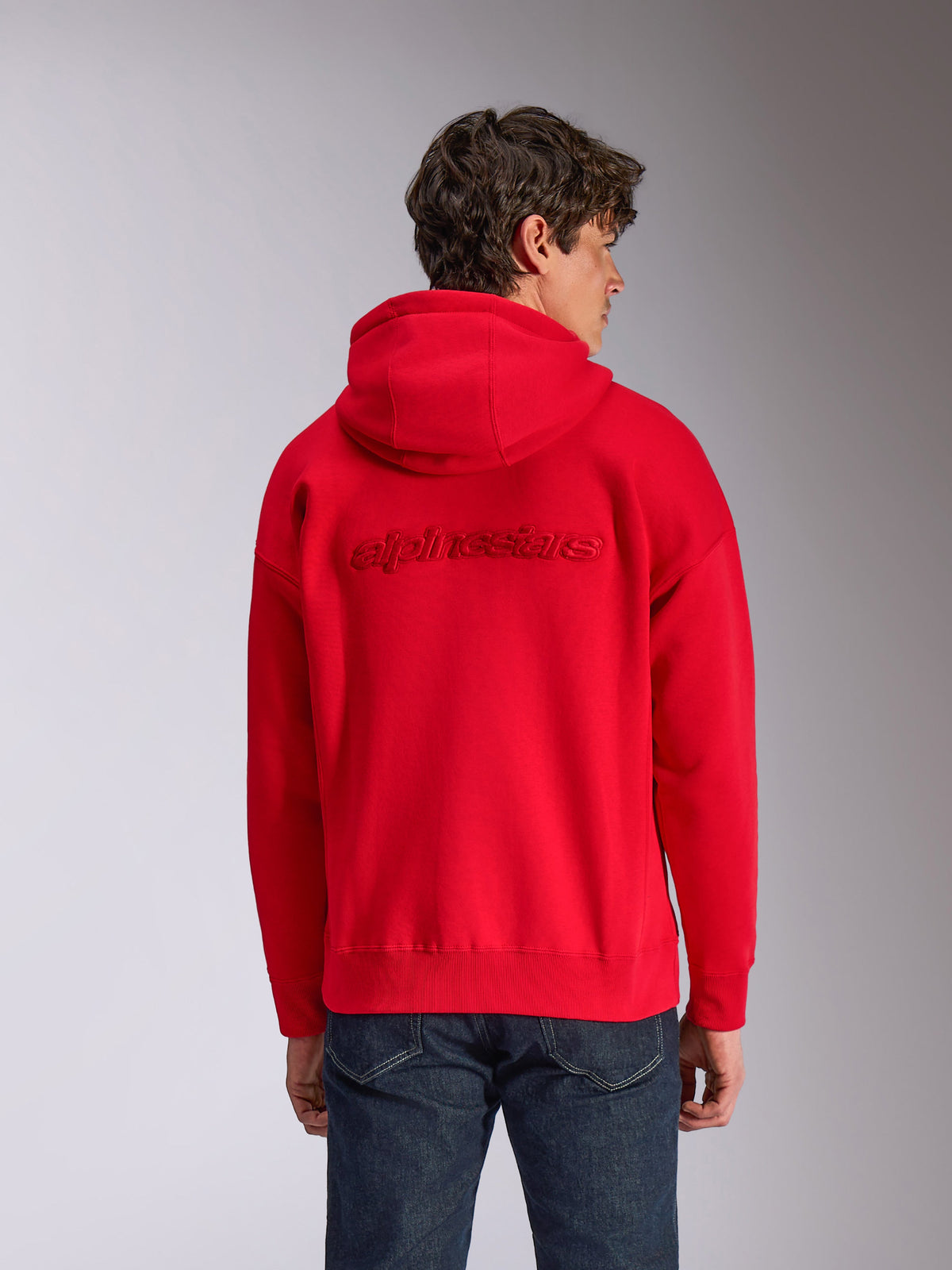 Sweat à capuche Alpinestars Emergent Oversized, rouge, vue de dos sur mannequin, avec logo Alpinestars brodé en 3D ton sur ton, coupe ample avec bord-côtes aux poignets et à l'ourlet, style streetwear décontracté inspiré du sport automobile