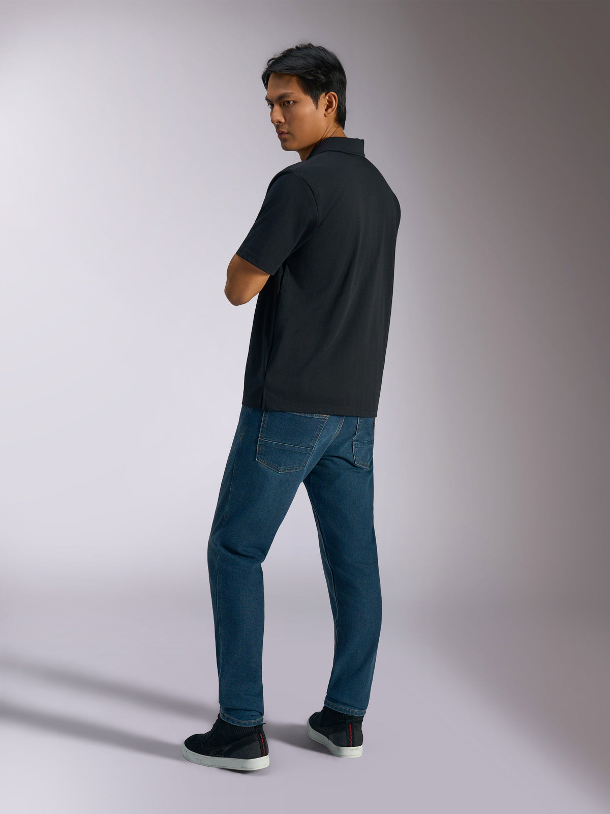 Polo Alpinestars Impetus Sport, noir, polo à manches courtes avec texture en maille imitation et patte à trois boutons, porté par un mannequin avec un jean bleu et des baskets noires, streetwear décontracté inspiré du sport automobile