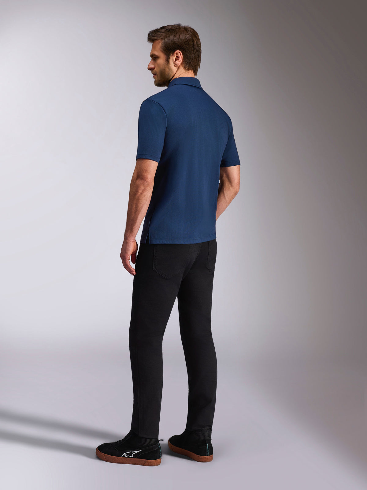 Polo Alpinestars Impetus Sport, polo bleu marine à manches courtes, vue de dos et de profil sur mannequin, associé à un pantalon noir et des baskets noires, vêtement de sport décontracté style motorsport