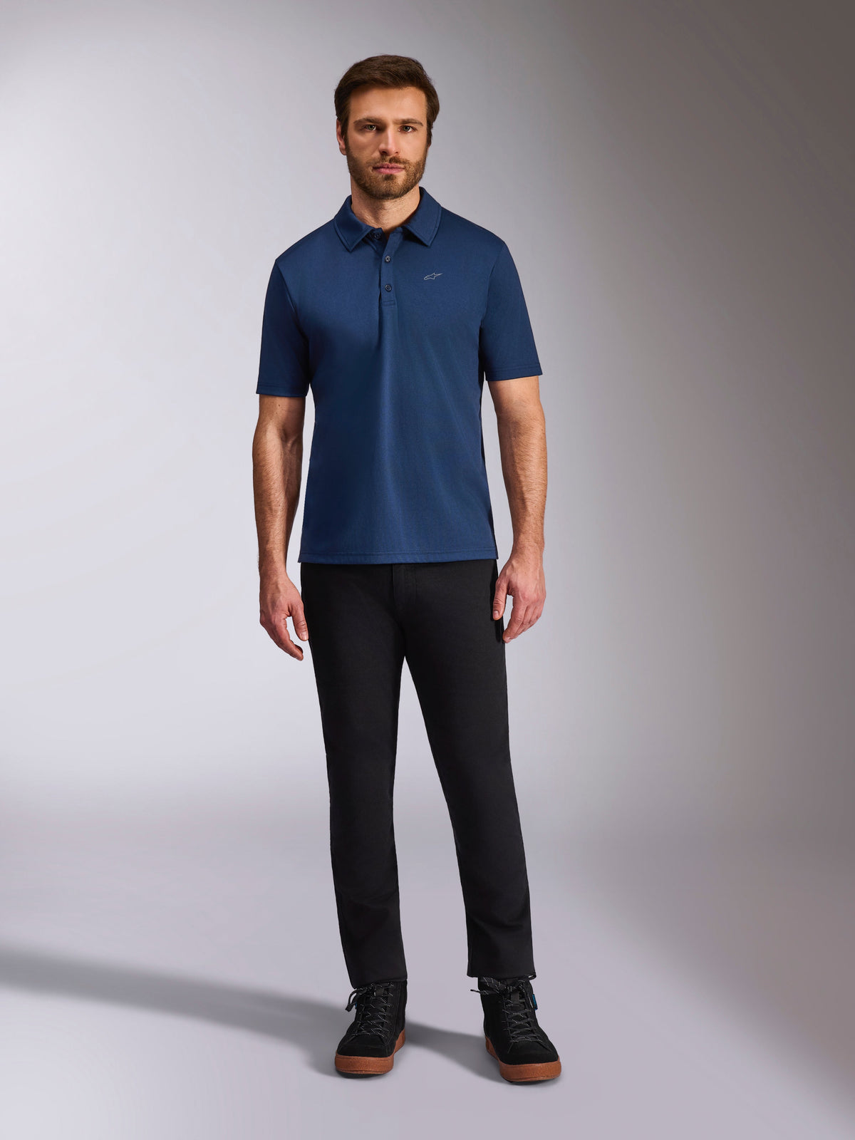 Alpinestars Polo Sport Impetus, polo à manches courtes, bleu marine, petit logo Astars argenté sur la poitrine, patte à trois boutons, porté par un mannequin avec un pantalon noir et des bottines, vêtement de sport décontracté inspiré du sport automobile