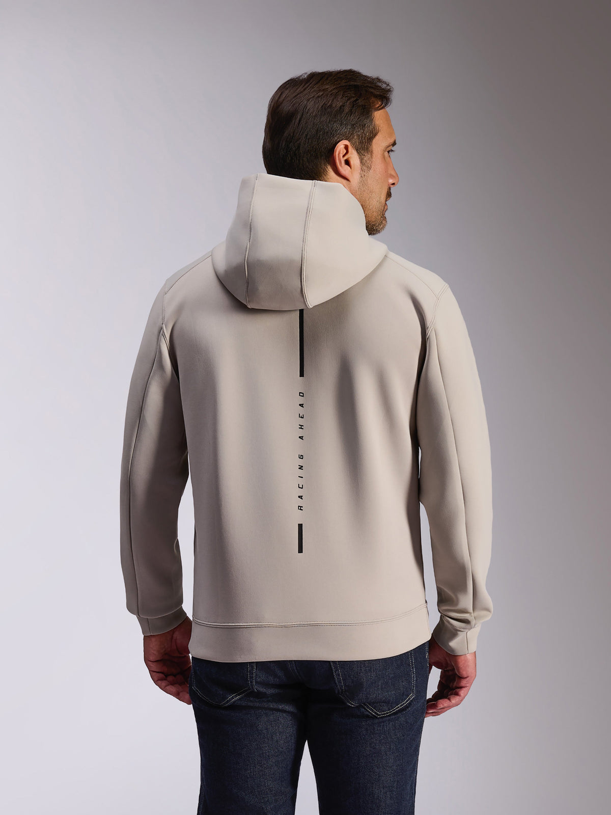 Alpinestars Insight Hoodie in Cement, back view of model wearing a light gray pullover sweatshirt, features a black vertical stripe logo with 'RACING AHEAD' text, casual motorsport-inspired double face fleece hoodie.