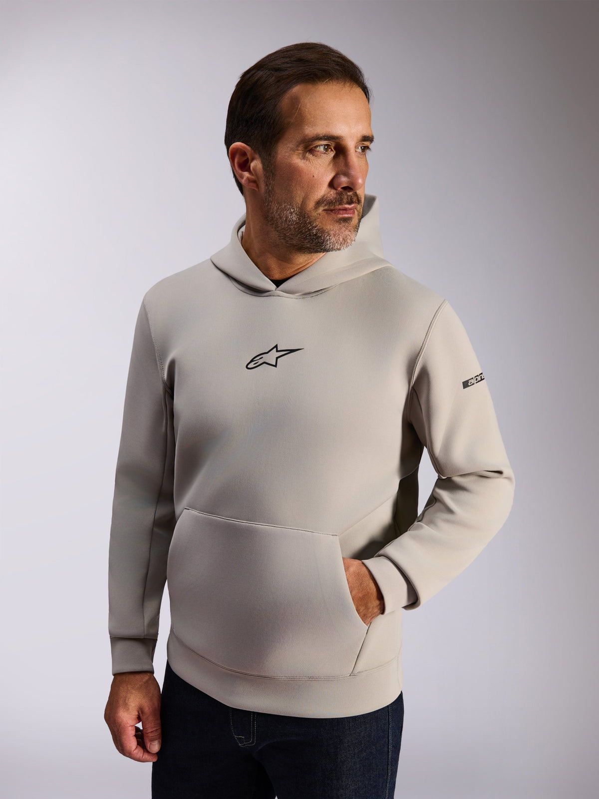 Sweat à capuche Alpinestars Insight, vêtement streetwear décontracté, polaire gris ciment, logo Astars noir à l'avant, poche kangourou, lettrage sur la manche, capuche doublée en mesh, vêtement moderne inspiré des sports mécaniques
