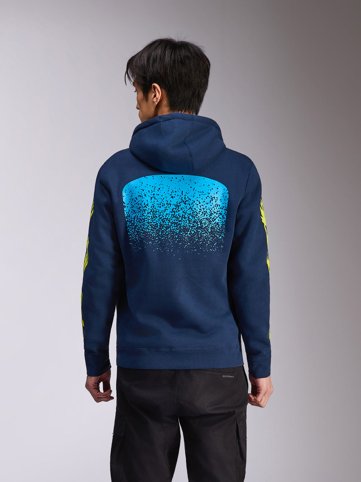 Sweat à capuche Alpinestars Obsessed, polaire à capuche bleu marine, vue de dos avec un grand graphisme dégradé MX bleu clair, logos Alpinestars jaunes sur les manches, streetwear décontracté inspiré des sports mécaniques