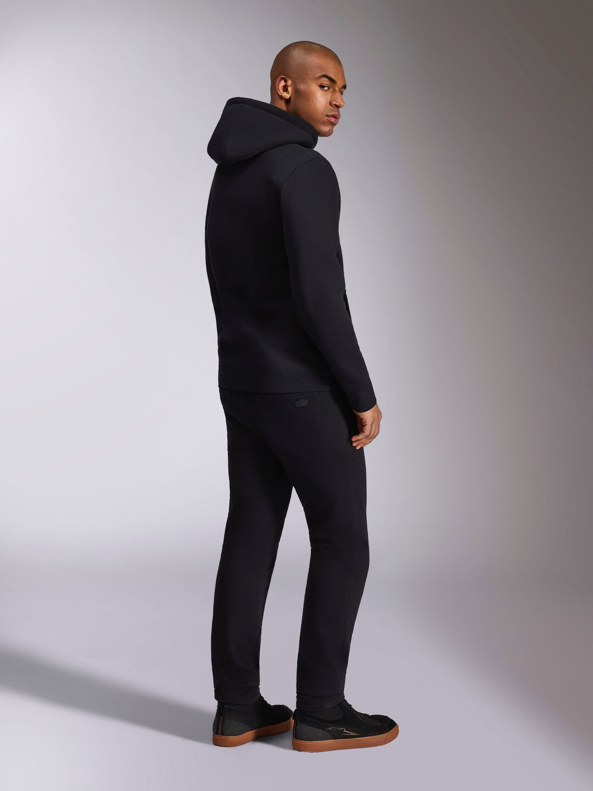 Alpinestars Ellipsoid Hoodie, black casual streetwear, back view on male model, hooded pullover fleece with rib cuffs and hem, worn with black pants and sneakers, modern motorsport-inspired design