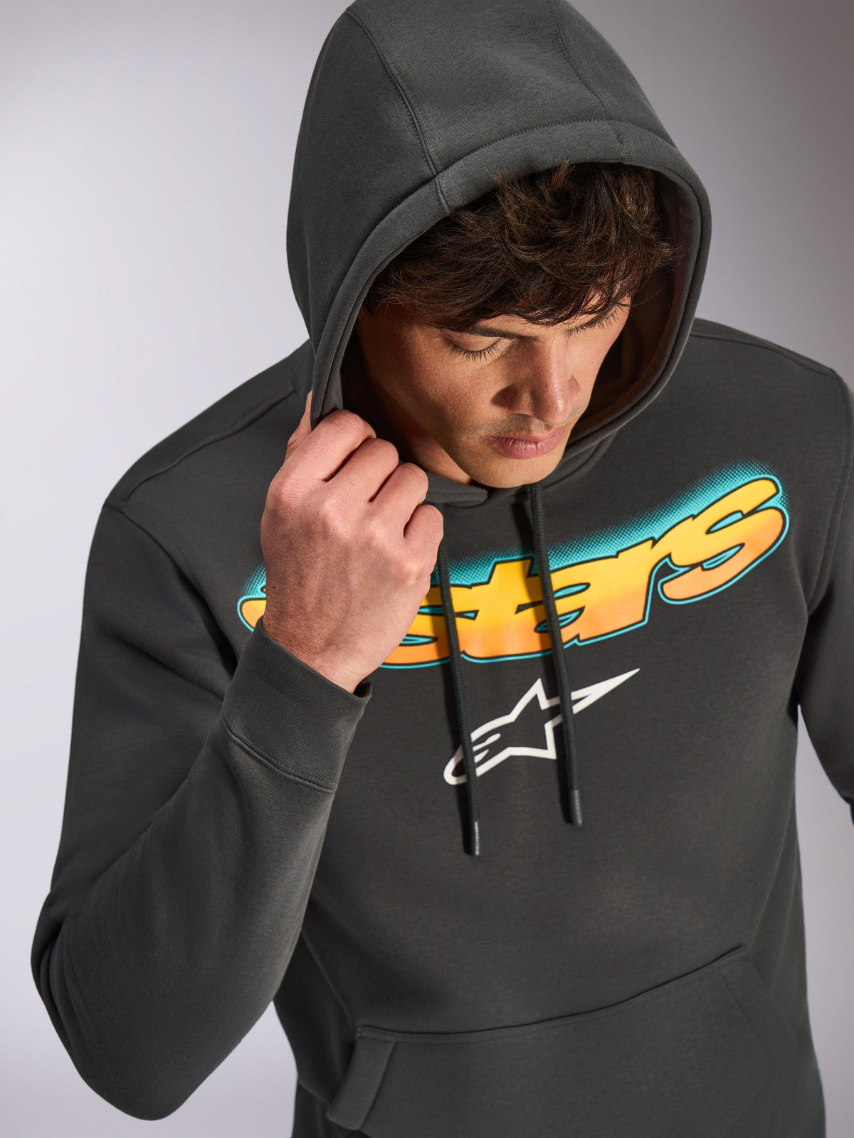 Alpinestars Ellipsoid Hoodie, gris gunmetal, sweat à capuche décontracté avec inscription Astars dégradée du cyan à l'orange et logo blanc, porté par un mannequin avec la capuche relevée, streetwear d'inspiration motorsport