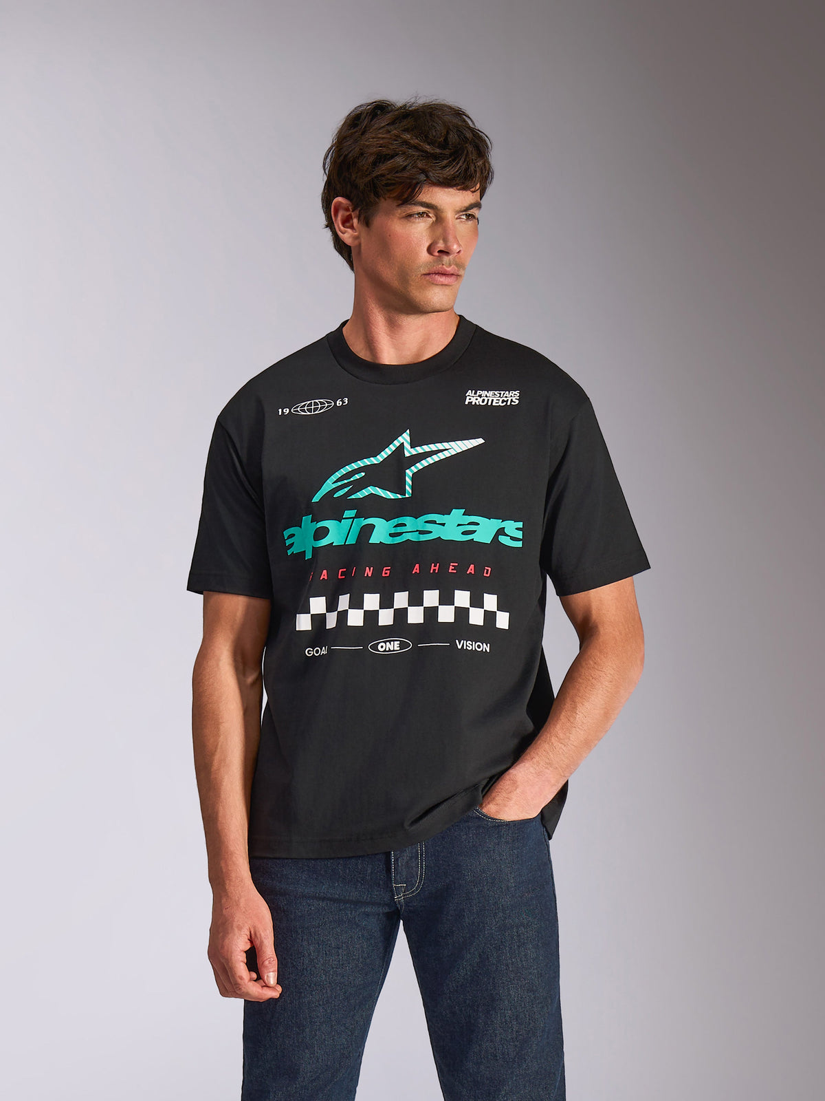 T-shirt Alpinestars Aplomb Oversized CSF, t-shirt à manches courtes, noir, avec un grand logo combo Astars bleu sarcelle et blanc et un motif à damier, porté par un mannequin homme avec un jean bleu foncé, streetwear motorsport décontracté