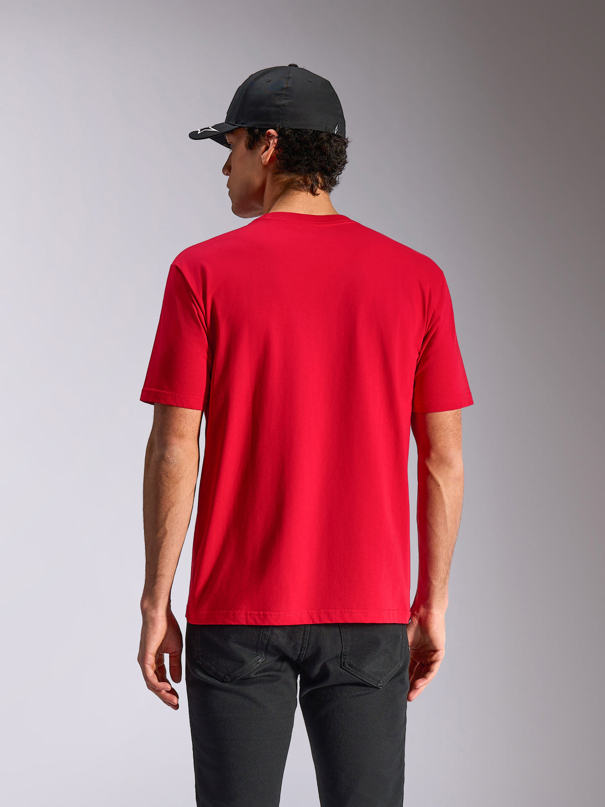 T-shirt Alpinestars Noka CSF, t-shirt à manches courtes, rouge, vue de dos sur mannequin, style streetwear décontracté inspiré du sport automobile, porté avec une casquette noire et un pantalon sombre