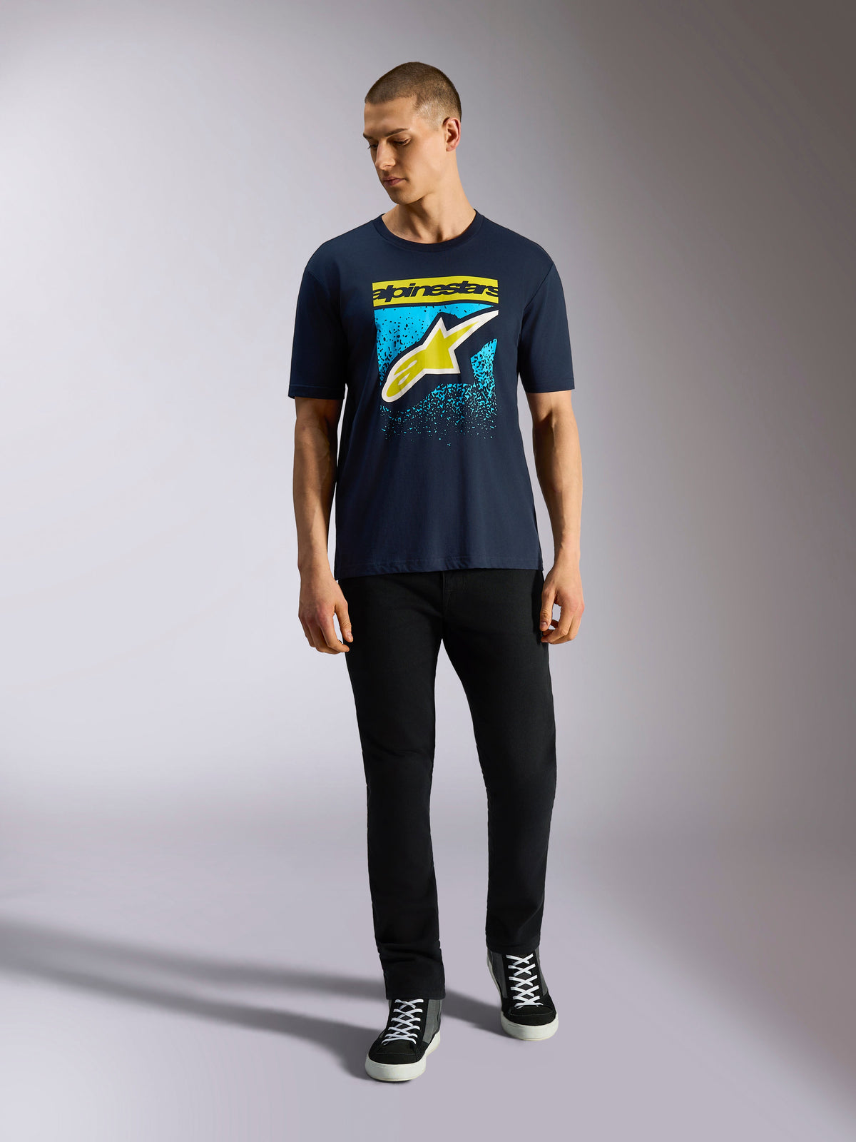 T-shirt à manches courtes Alpinestars Noka CSF, bleu marine, logo Astars à l'avant avec dégradé MX jaune et bleu clair, porté par un mannequin avec un pantalon noir, style streetwear décontracté