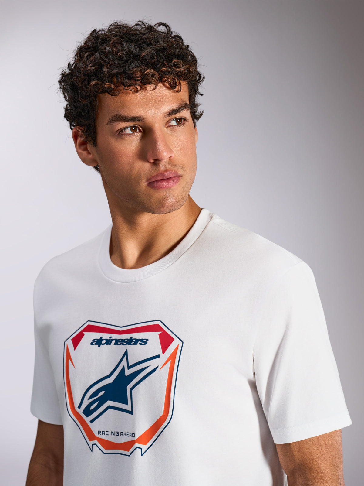 Alpinestars Plate CSF Tee, t-shirt à manches courtes, blanc, avec un graphique de plaque Astars MX à l'avant et des accents rouges et orange, texte « Racing Ahead », porté par un mannequin, streetwear de sport automobile décontracté