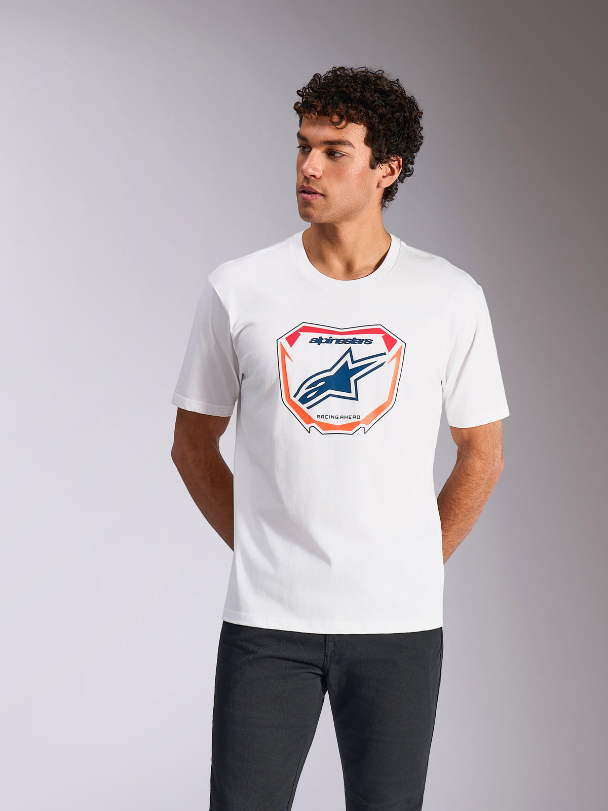T-shirt Alpinestars Plate CSF, t-shirt à manches courtes, blanc, avec graphique de plaque Astars MX à l'avant, logo bleu et bordure orange, porté par un mannequin, streetwear de sport automobile décontracté
