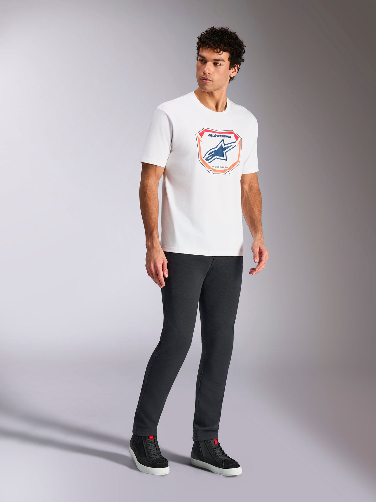 Alpinestars Plate CSF Tee, t-shirt à manches courtes, blanc, avec graphique frontal de plaque Astars MX en bleu et orange, tenue streetwear décontractée d'inspiration sport automobile portée avec un pantalon sombre et des baskets montantes