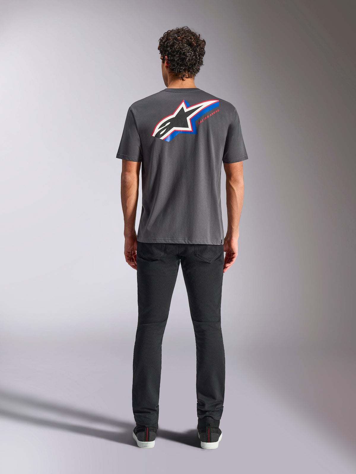 T-shirt Alpinestars Angler CSF, t-shirt à manches courtes, anthracite, grand logo Astars multicolore au dos avec des accents rouges et bleus, vue de dos sur modèle, streetwear décontracté inspiré du sport automobile