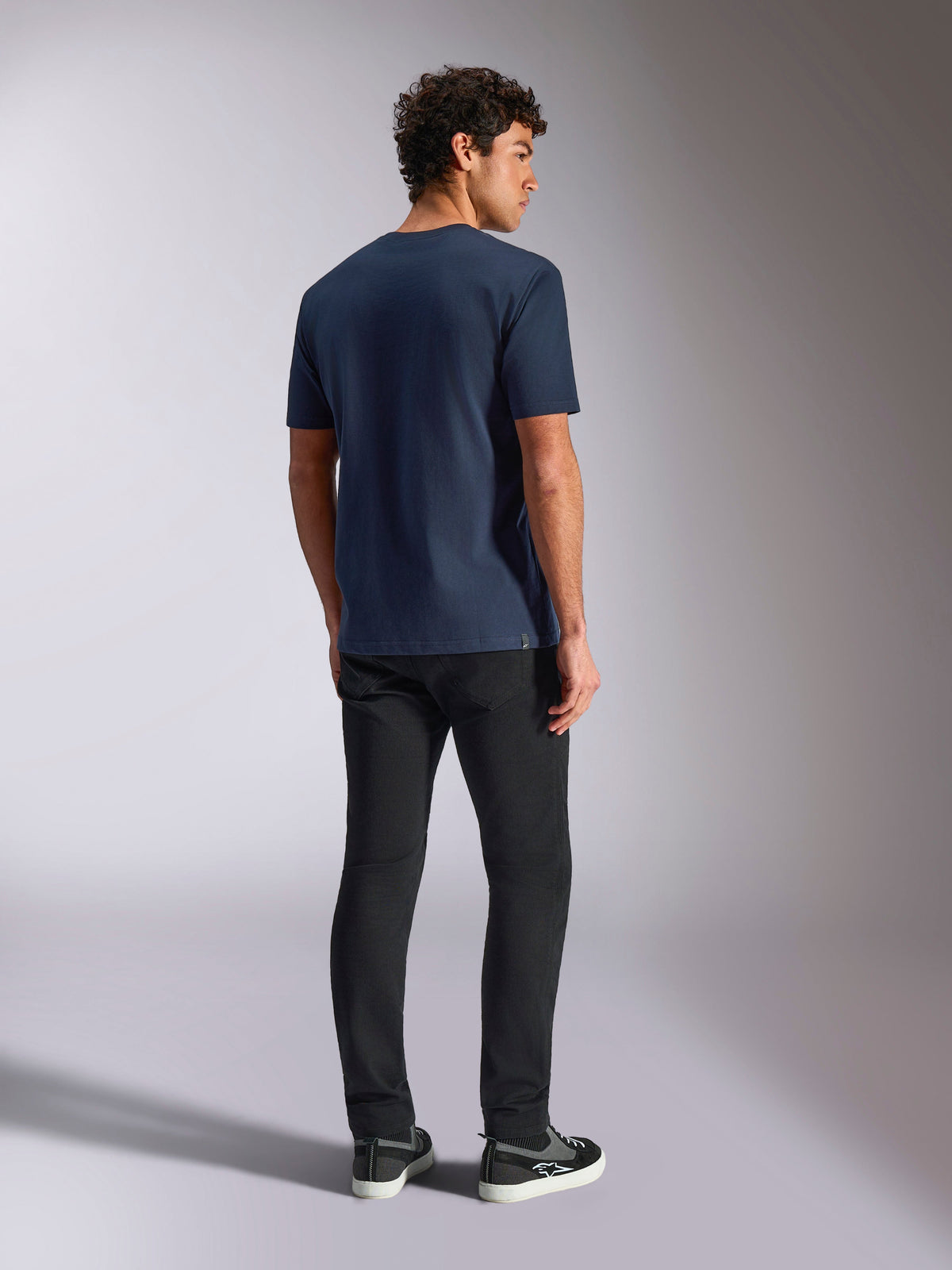 T-shirt Alpinestars Trifecta CSF, manches courtes, bleu marine, vue de dos, style sportswear décontracté, porté avec un pantalon noir et des baskets noires