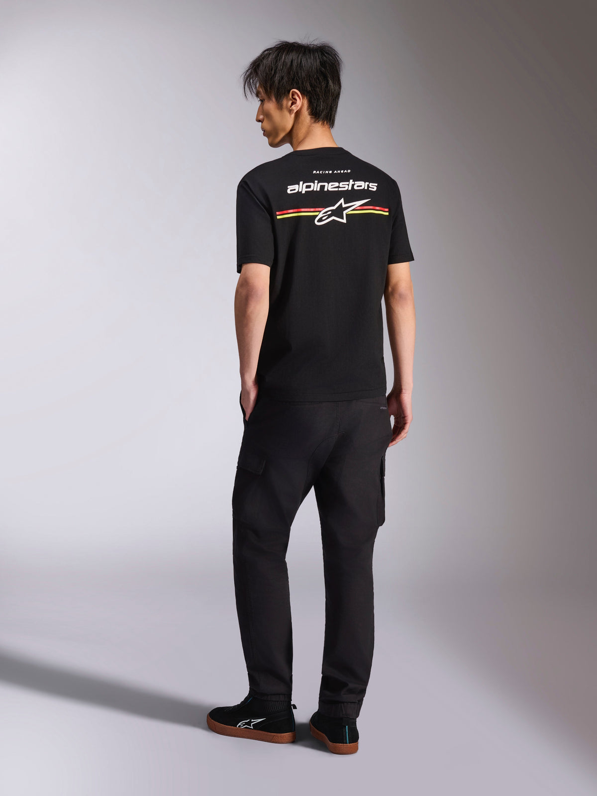 T-shirt Alpinestars Lanes CSF, t-shirt noir à manches courtes, vue de dos avec logo Alpinestars blanc et rayures graphiques rouges, orange et jaunes, look streetwear motorsport décontracté avec pantalon cargo noir