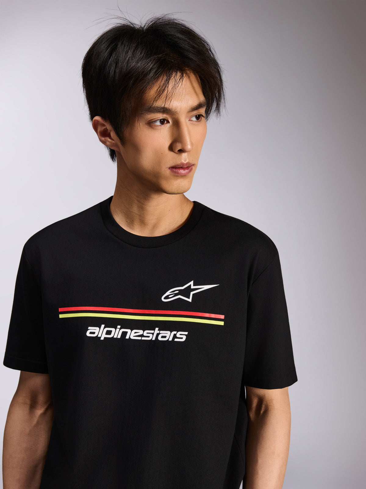 T-shirt Alpinestars Lanes CSF, t-shirt à manches courtes, noir, avec logos Astars et Alpinestars blancs et rayures rouges et jaunes, streetwear décontracté porté par un mannequin