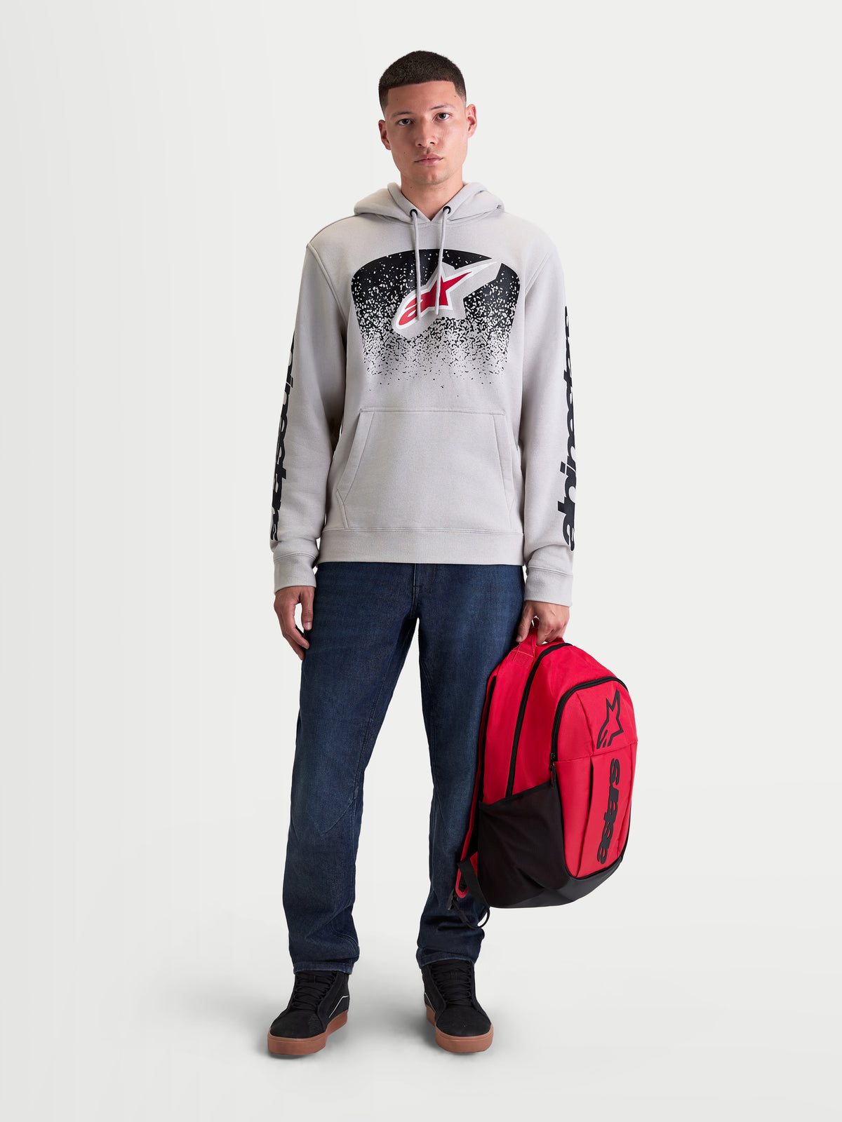 Alpinestars sac à dos GFX Boss, sac à dos sportswear de 20L, rouge et noir, en polyester 600D durable avec logo Astars en silicone en relief, tenu par un modèle homme pour un style urbain quotidien.