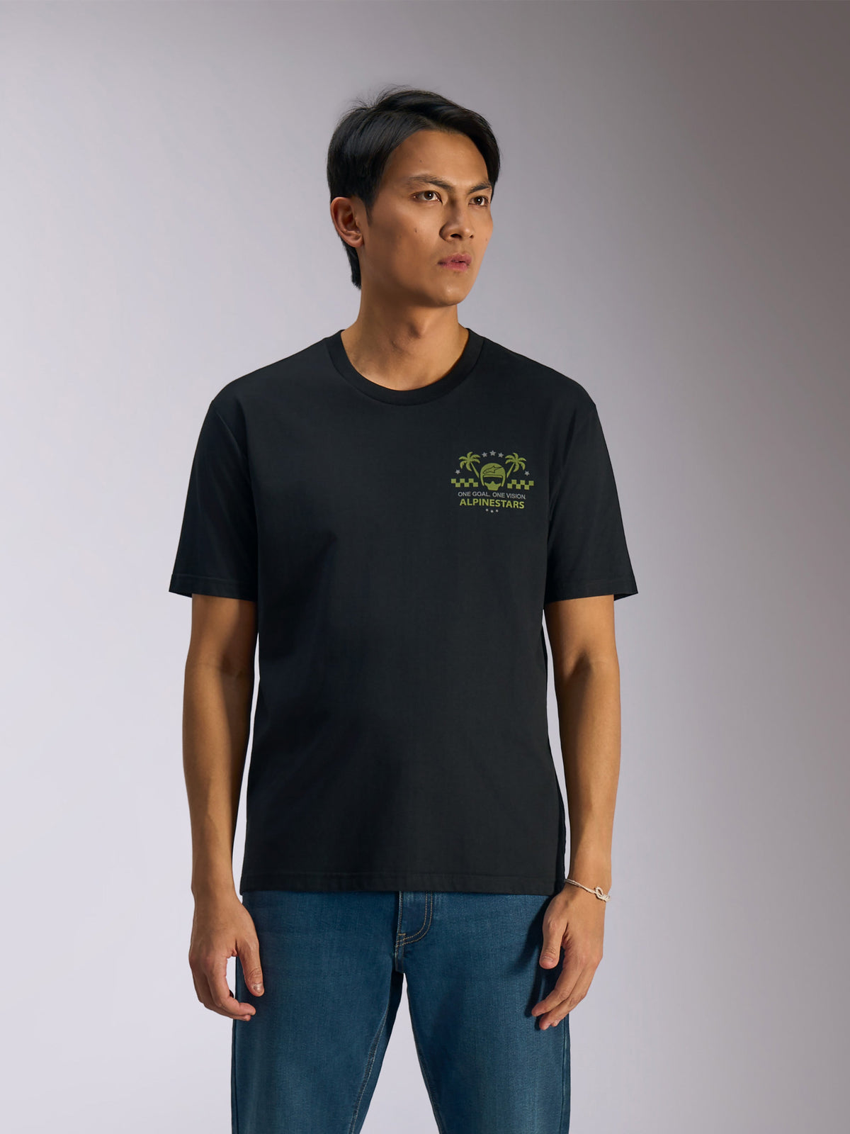 T-shirt Alpinestars Order CSF, t-shirt à manches courtes, noir, graphisme vert avec casque et palmiers sur la poitrine, porté avec un jean bleu, streetwear décontracté motorsport