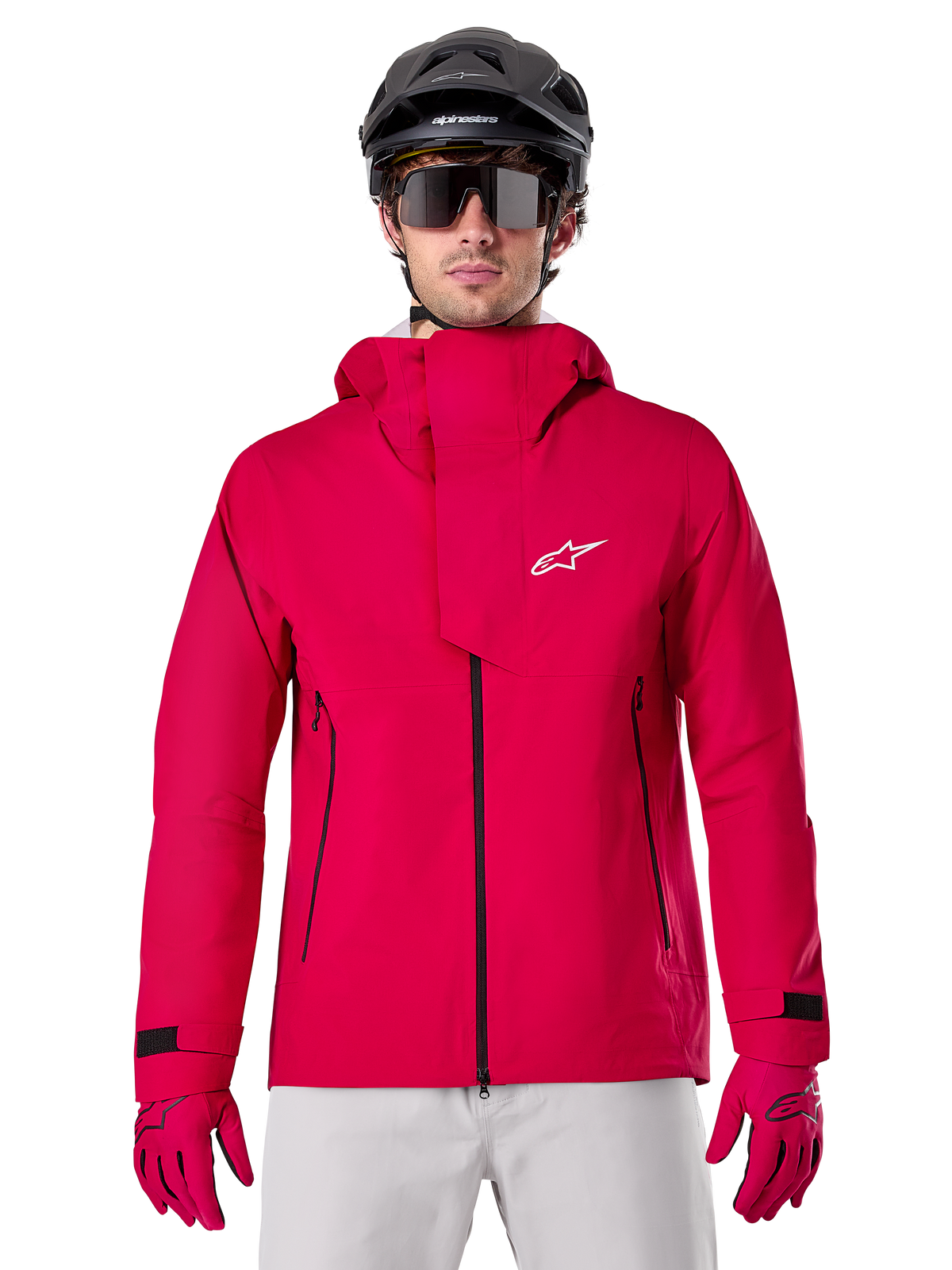 Alpinestars A-Dura Elite Waterproof Jacket, veste de pluie pour VTT, rouge fluo, col montant avec logo Alpinestars blanc, fermetures éclair noires, portée avec gants assortis et casque de vélo noir, équipement de cyclisme technique imperméable