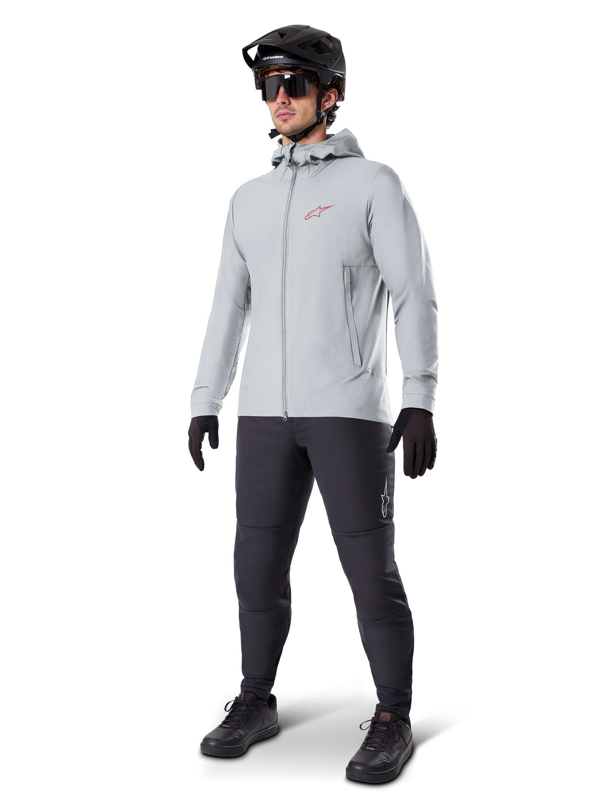 Veste thermique Alpinestars A-Dura en Titanium, veste de cyclisme à capuche gris clair avec logo Alpinestars rouge sur la poitrine, portée par un homme avec casque de VTT noir, lunettes de soleil, pantalon gris foncé et gants noirs, équipement de VTT professionnel