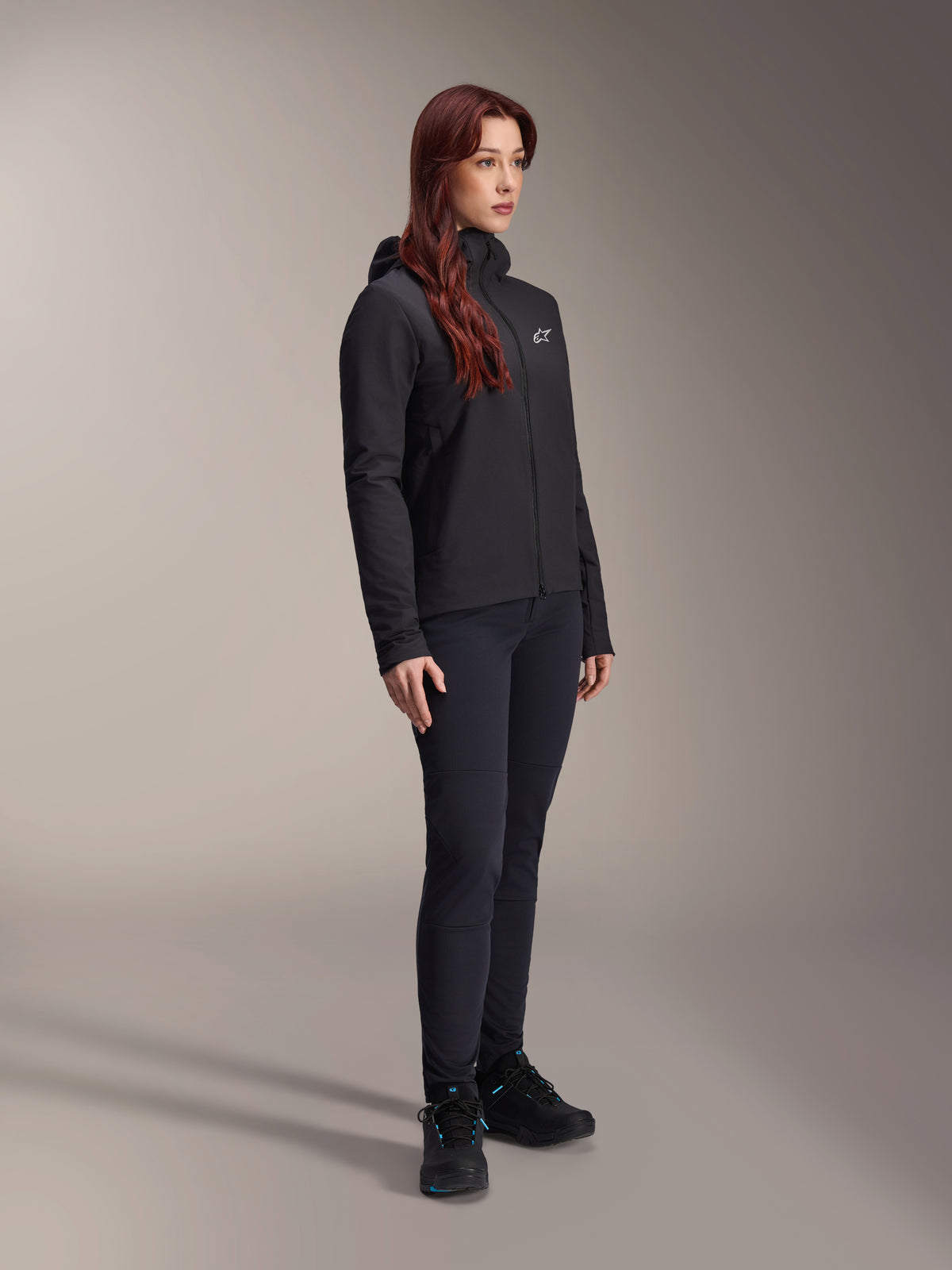 Veste thermique Alpinestars Stella A-Dura, veste isolante légère noire pour femme avec capuche, portée avec un pantalon noir et des chaussures noires, tenue de cyclisme et de VTT professionnelle pour conditions froides