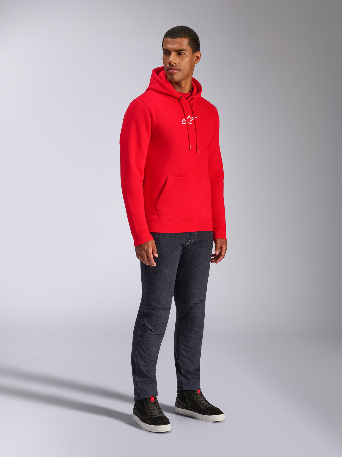 Alpinestars Frontal Hoodie, Red, male model wearing pull-over fleece hoodie with white A-star chest logo, kangaroo pocket, drawstring hood, paired with dark denim jeans, casual motorsport-inspired streetwear