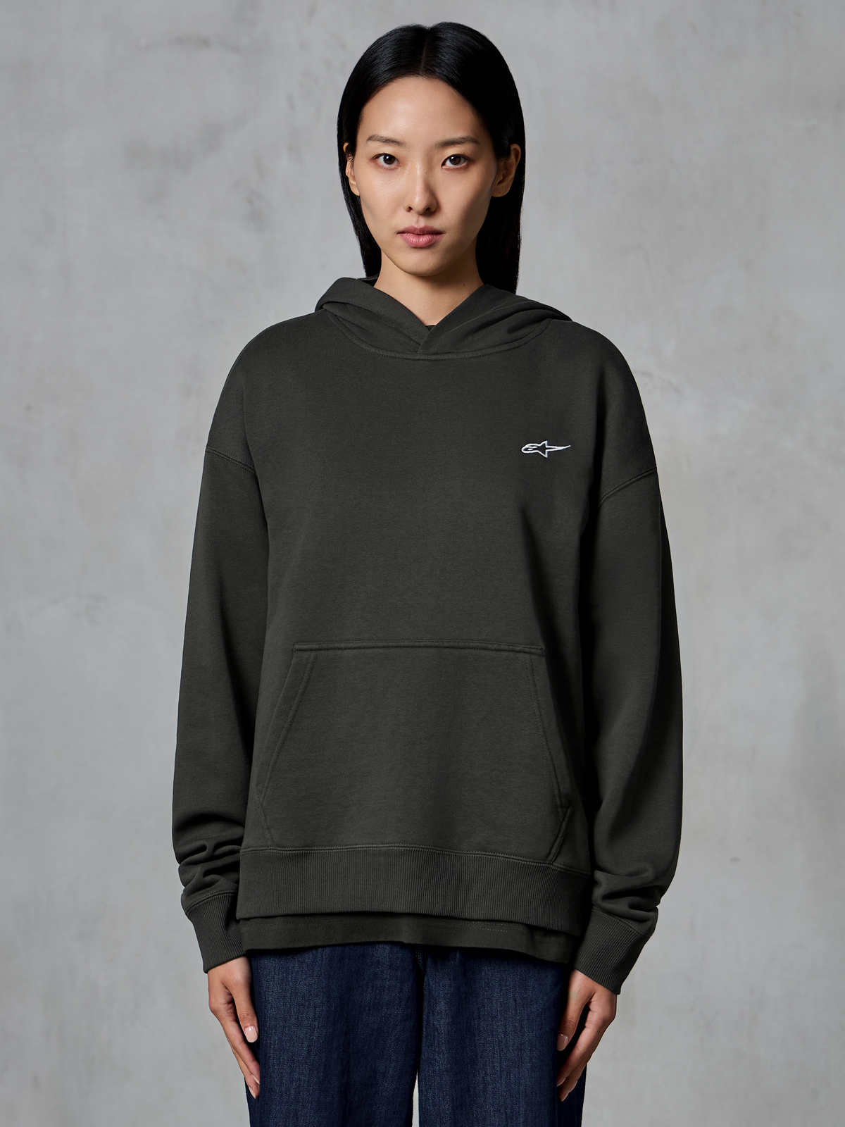 Sweat à capuche Alpinestars Essentials Ageless, Off Black, porté par un mannequin, arborant un petit logo Astars blanc sur la poitrine, poche kangourou à l'avant, finition délavée à la pierre, streetwear décontracté en molleton de qualité supérieure