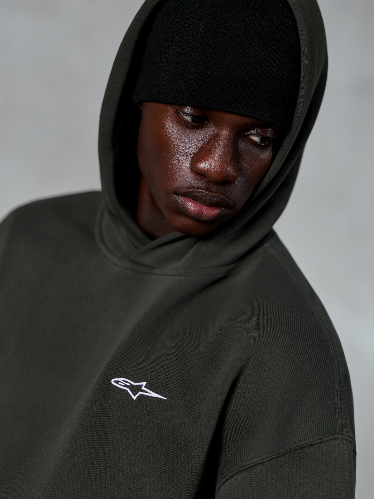 Sweat à capuche Alpinestars Essentials Ageless, Off Black, gros plan d'un mannequin portant un bonnet noir sous la capuche, arborant un petit logo étoile blanc sur la poitrine, streetwear décontracté inspiré des sports mécaniques