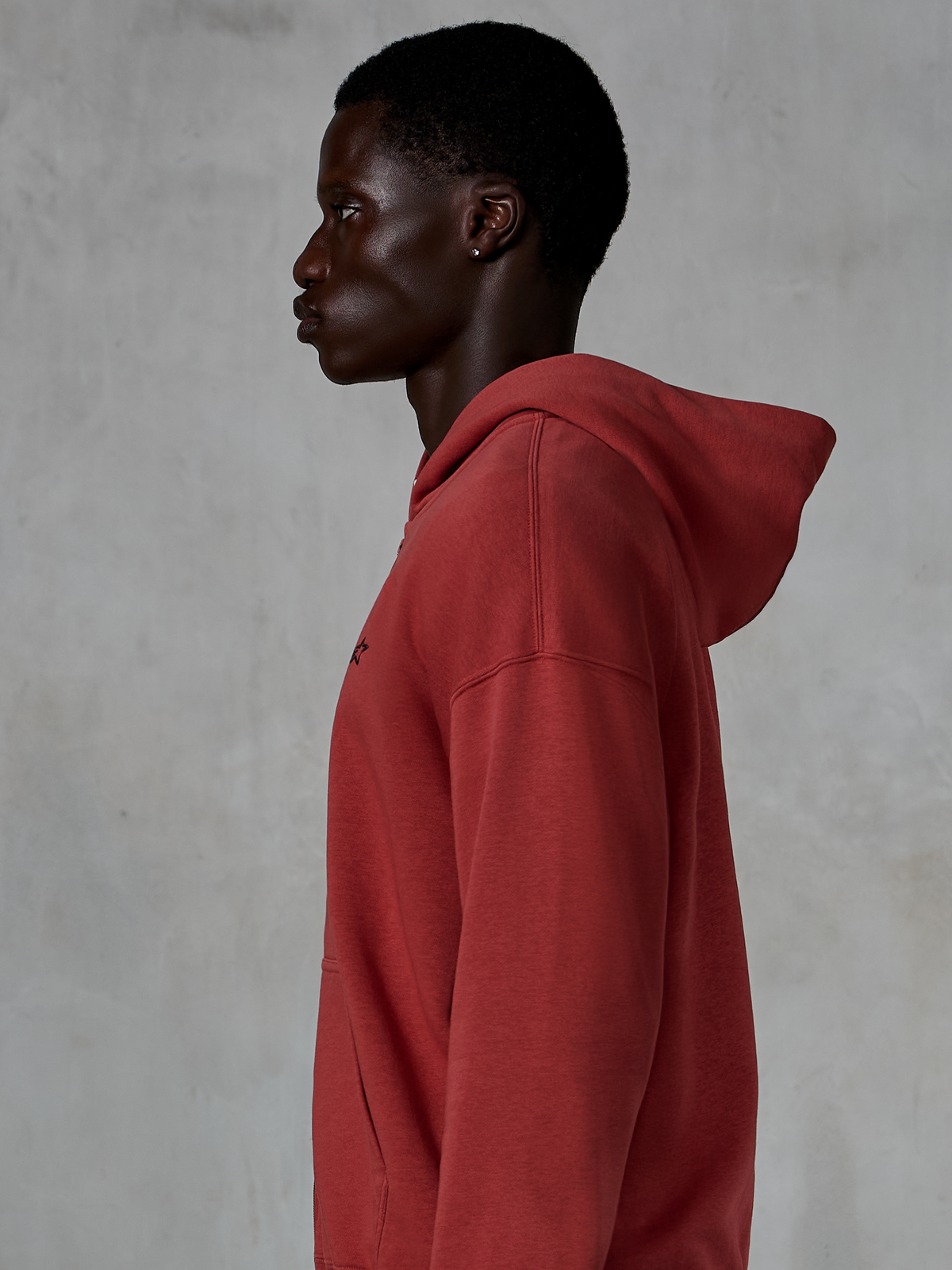 Sweat à capuche zippé Alpinestars Essentials Ageless, rouge brique, vue de profil d'un homme portant un sweat à capuche zippé à coupe décontractée, petit logo étoile noir sur la poitrine, polaire premium délavée à la pierre, streetwear décontracté inspiré du sport automobile