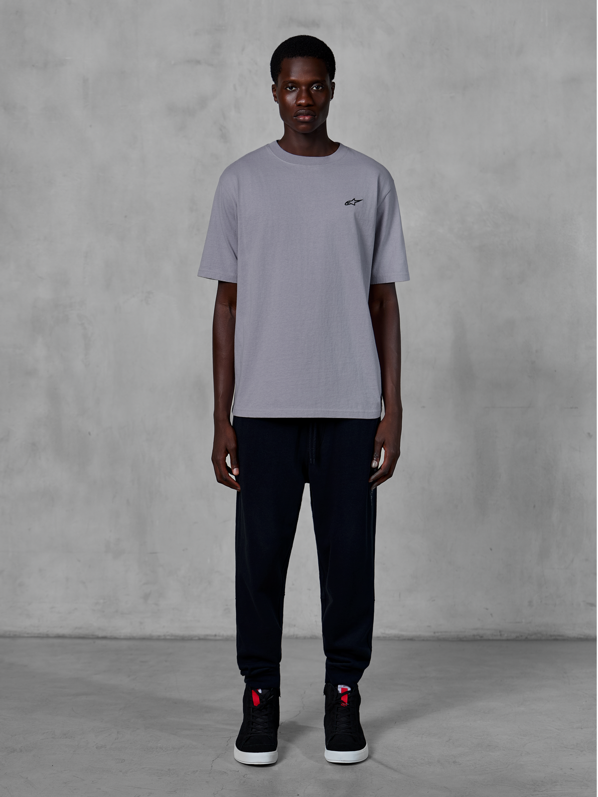 Alpinestars Essentials Ageless SS Tee, t-shirt à manches courtes, argent, avec un petit logo noir sur la poitrine, porté avec un jogging noir et des baskets, style streetwear décontracté inspiré du sport automobile