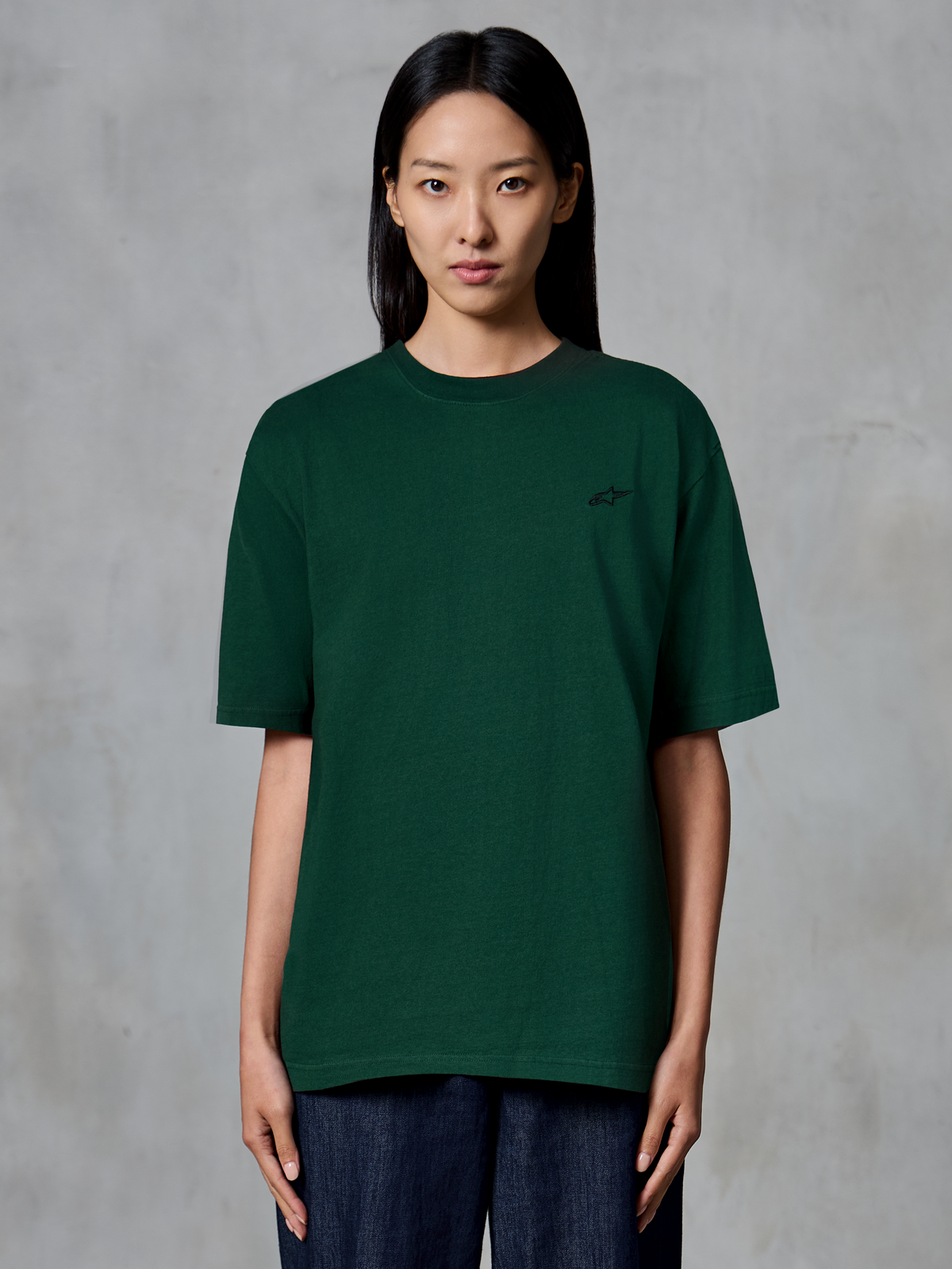 Alpinestars Essentials Ageless SS Tee, t-shirt à manches courtes, vert sapin, porté par un mannequin, avec un petit logo noir sur la poitrine, coupe décontractée, streetwear décontracté en coton biologique
