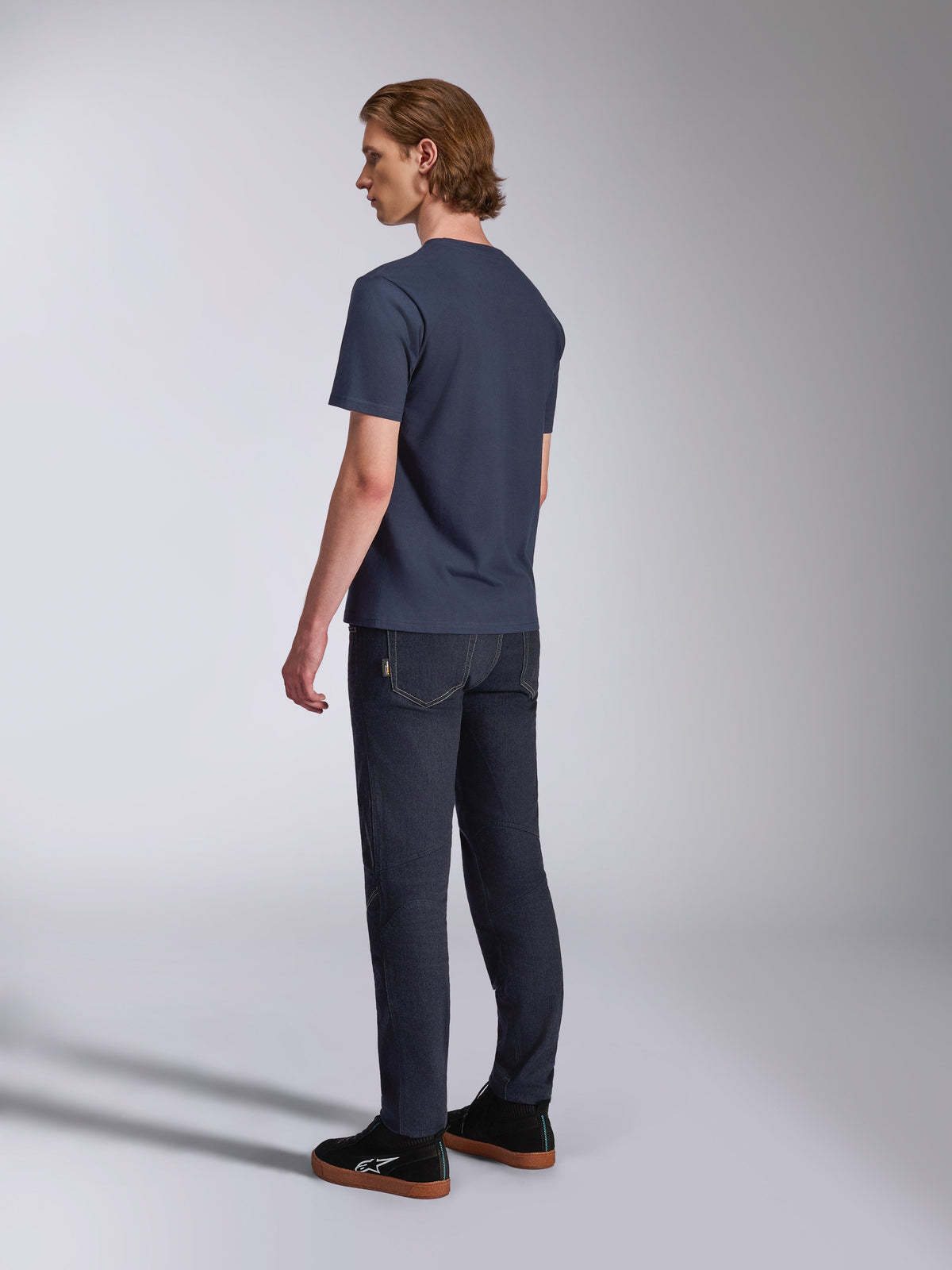 T-shirt Alpinestars Fasting CSF, t-shirt à manches courtes, bleu marine, vue arrière sur mannequin, associé à un pantalon en denim foncé et des baskets noires, style streetwear décontracté inspiré du sport automobile