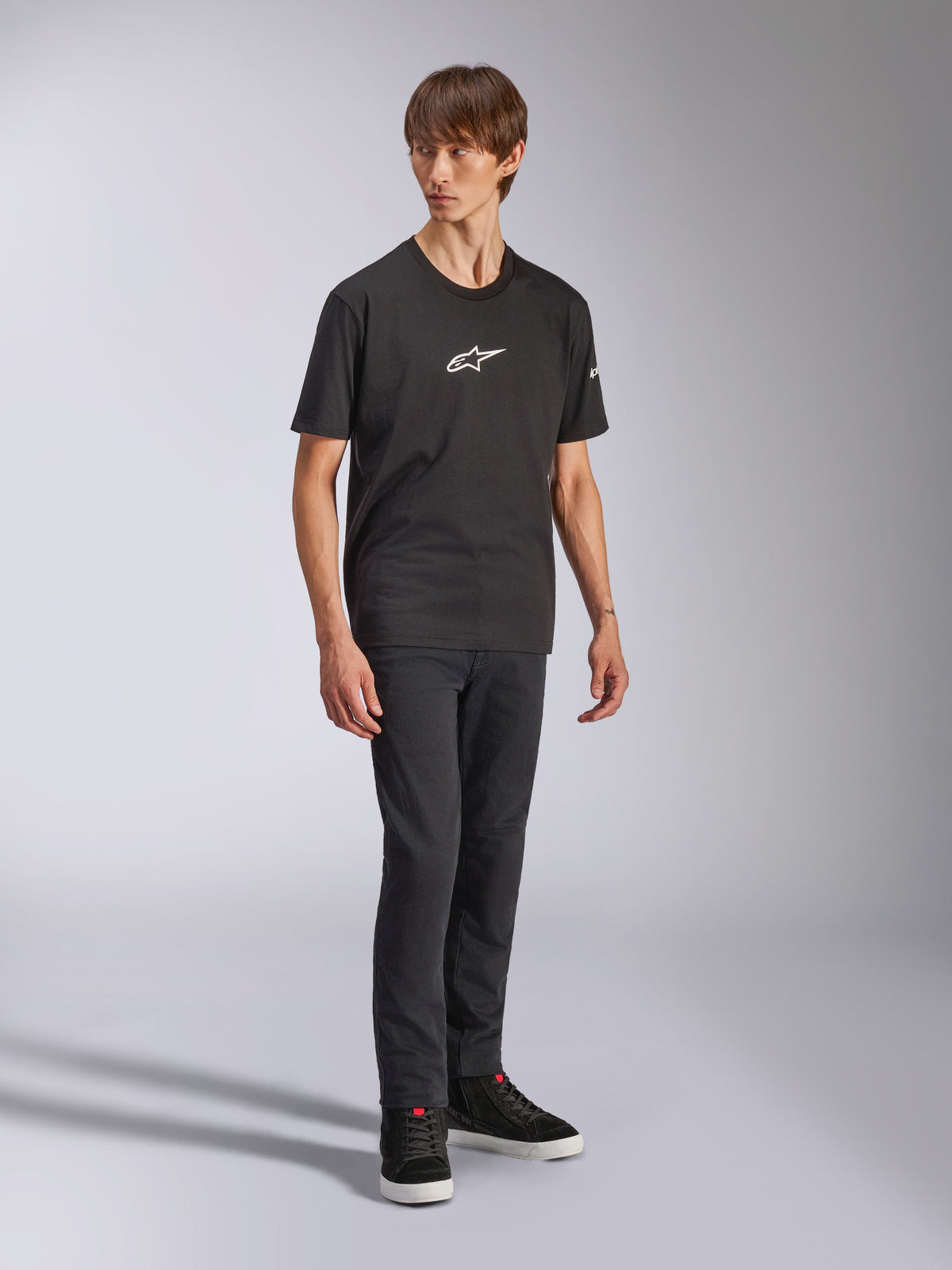 Alpinestars Frontal CSF Tee, t-shirt à manches courtes, noir, logo Astars blanc sur la poitrine, porté par un mannequin avec un jean foncé et des baskets noires, streetwear de performance décontracté