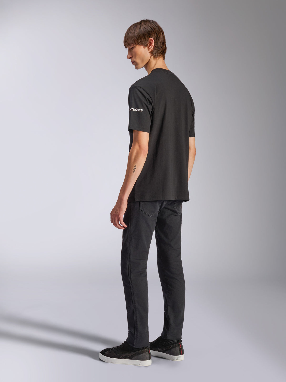 Alpinestars Frontal CSF Tee, Short Sleeve T-Shirt, Black, white astars branding on the sleeve, worn by model with black pants and shoes, casual motorsport-inspired design