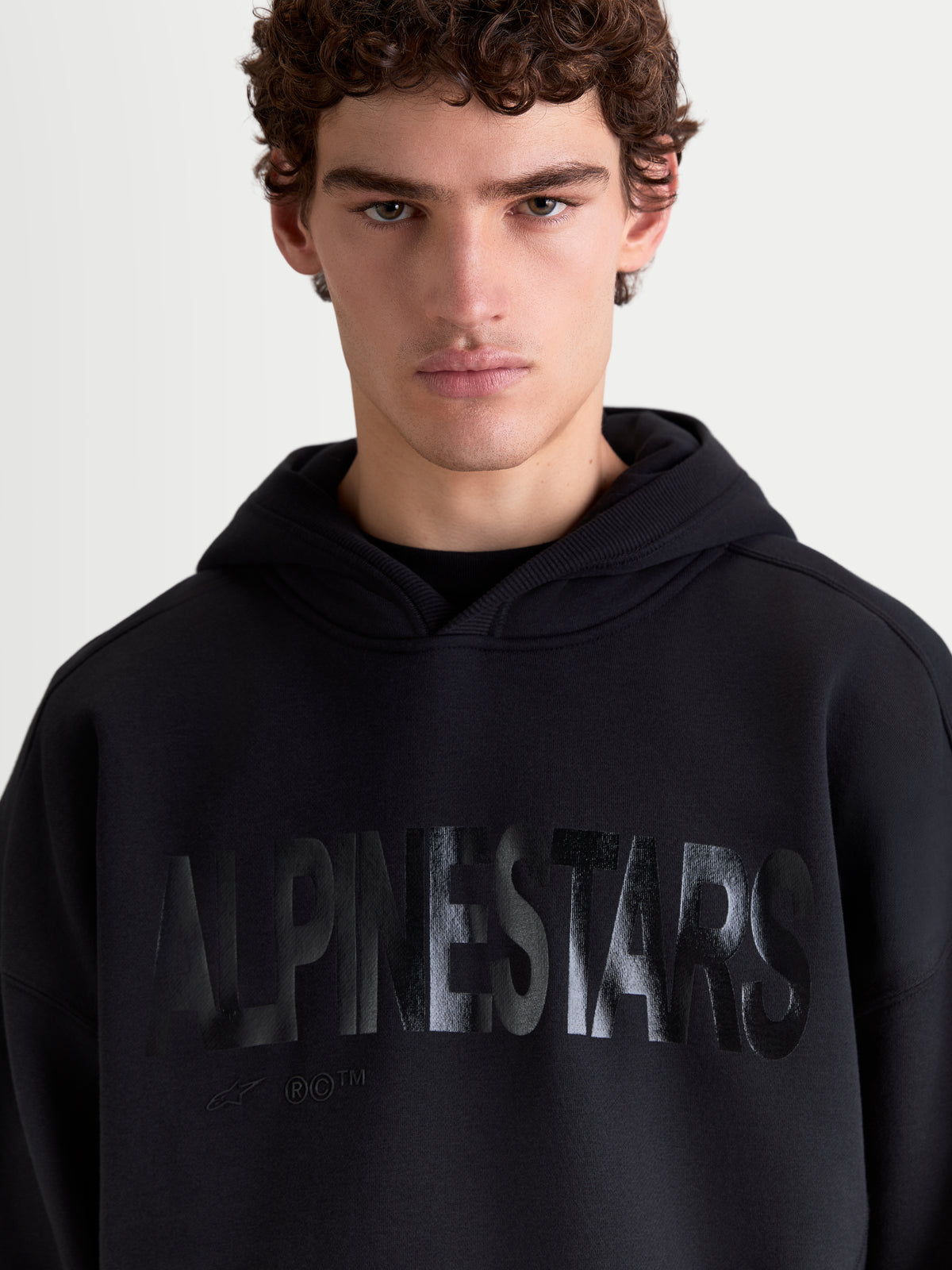 Alpinestars Shaw Oversized, sweat à capuche de sportswear pour homme et femme, noir, logo texturé ton sur ton sur la poitrine, coupe ample, polaire en mélange de coton, vue rapprochée sur modèle